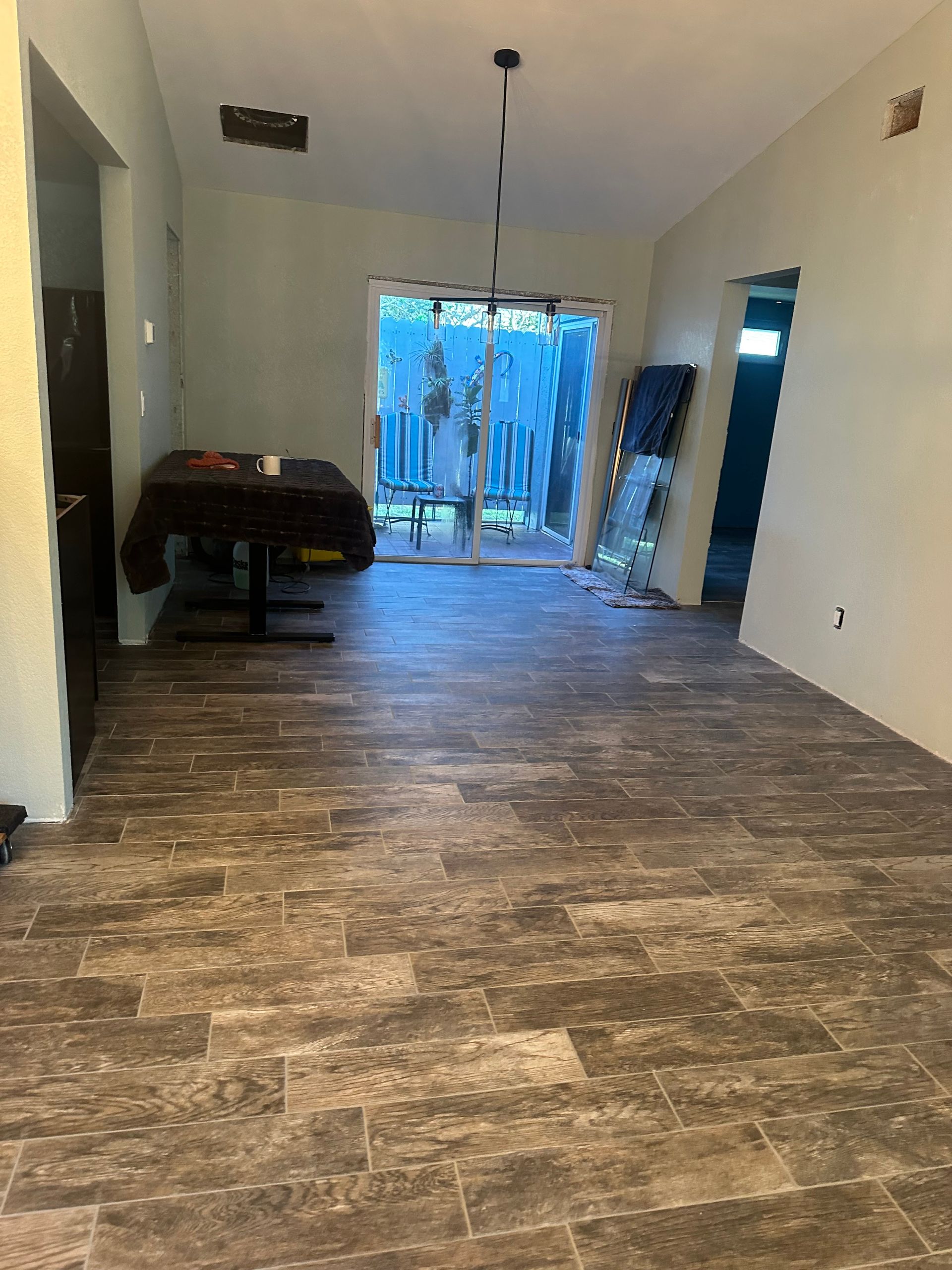 Room with new tile flooring, doorway to outside, partially finished walls, table, and open door.
