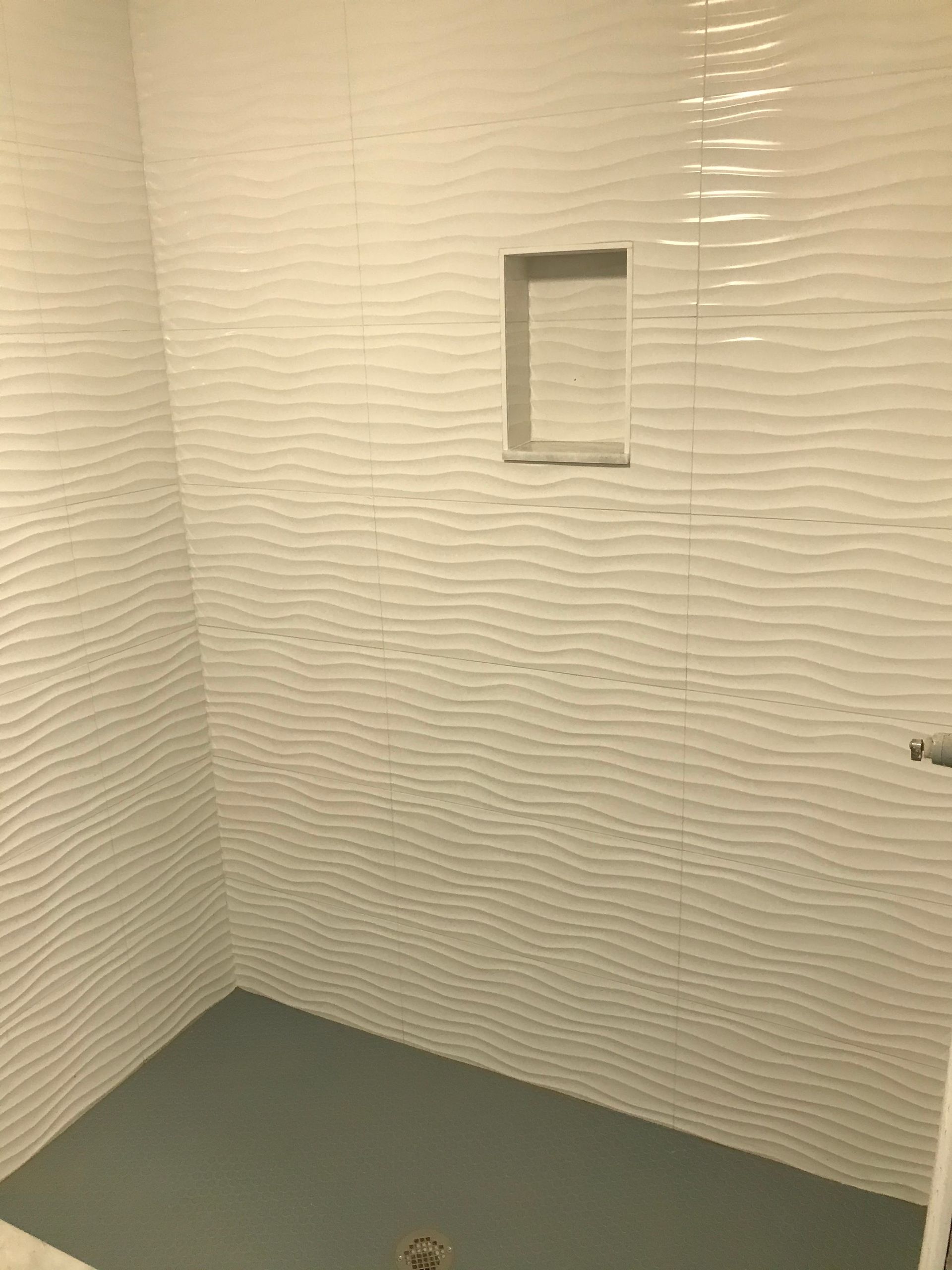 White tiled shower with a gray floor and built-in shelf.