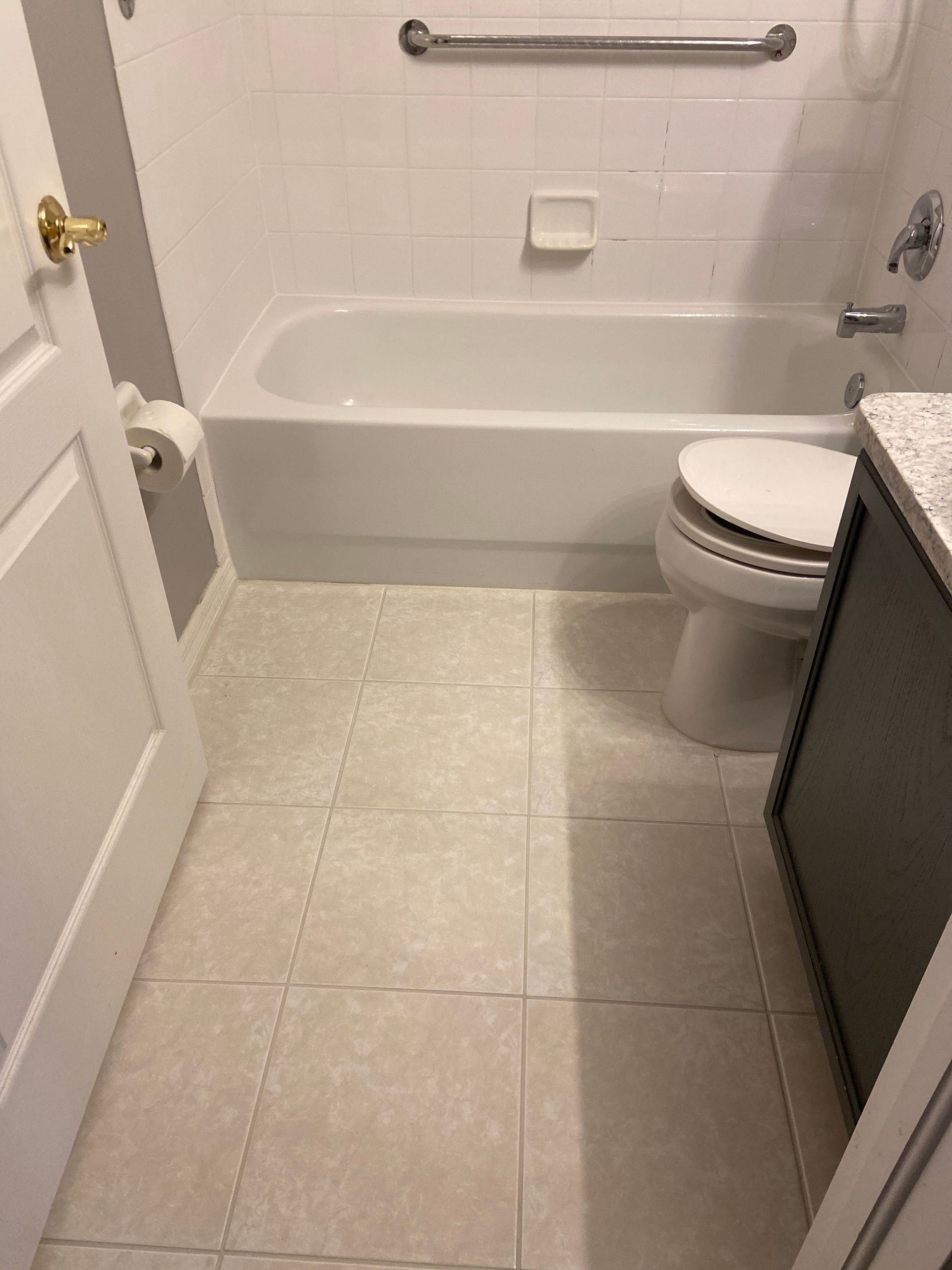 Bathroom with a white tub, toilet, and gray floor tiles.