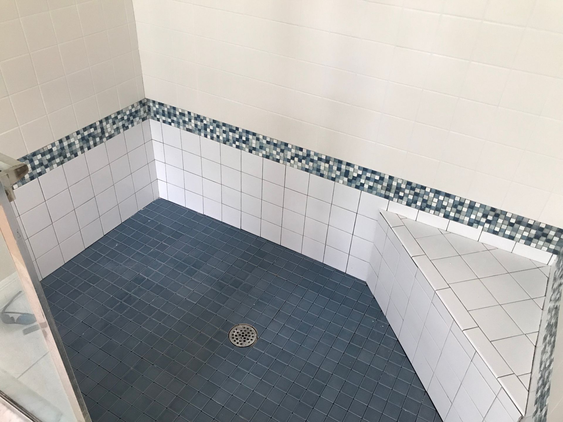 Tiled shower stall with blue floor and white walls, accented with blue mosaic border.