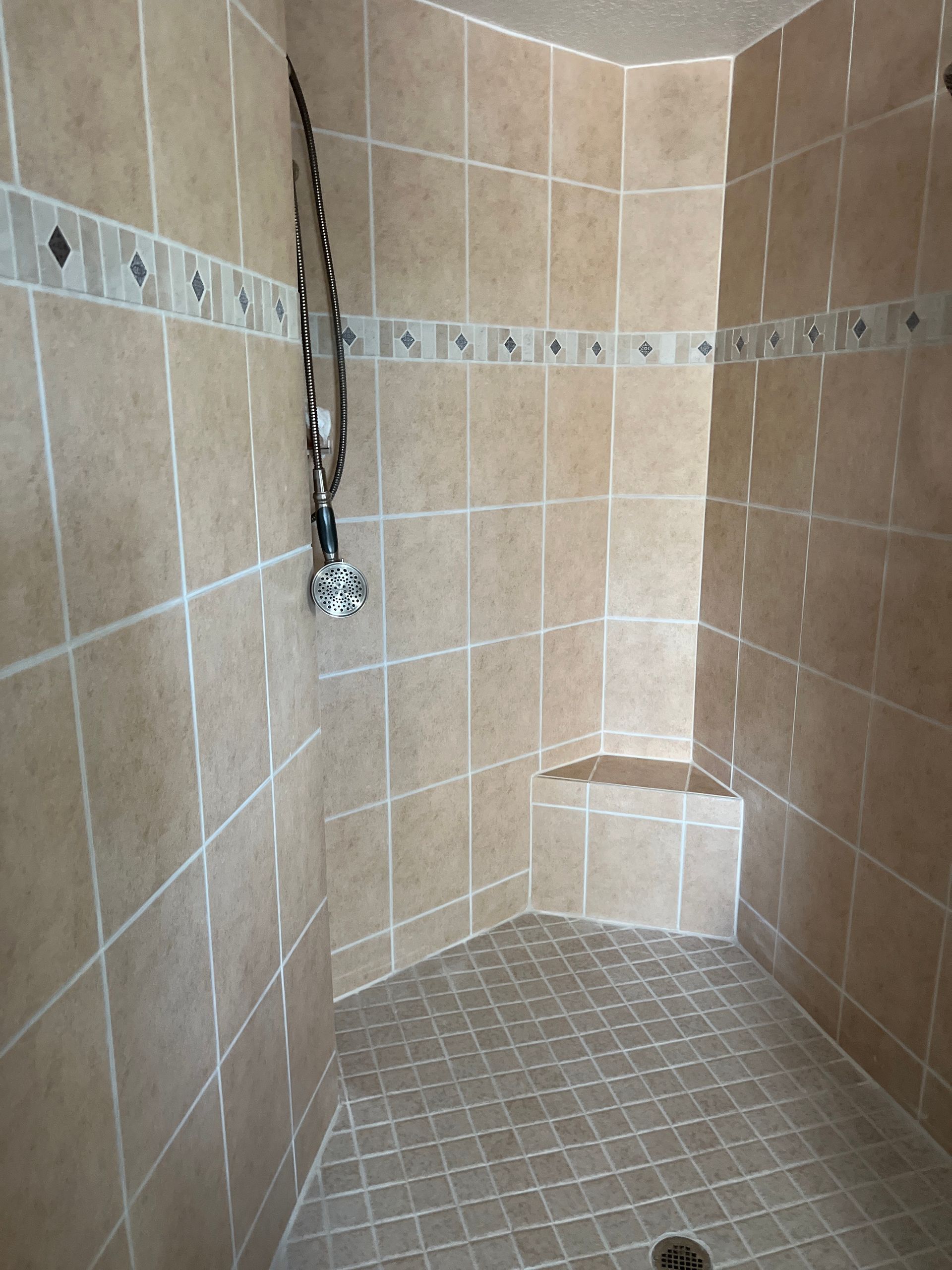 Shower with tan tiles, decorative tile border, built-in seat, and chrome showerhead.