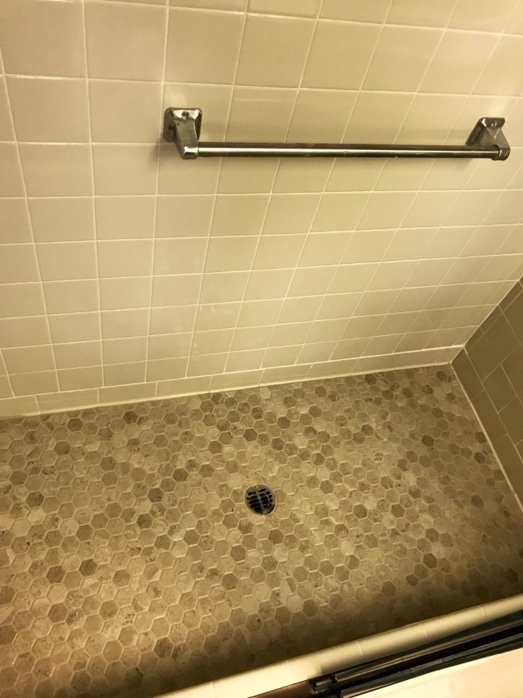A shower with tan hexagon floor tiles, beige wall tiles, and a silver towel bar.