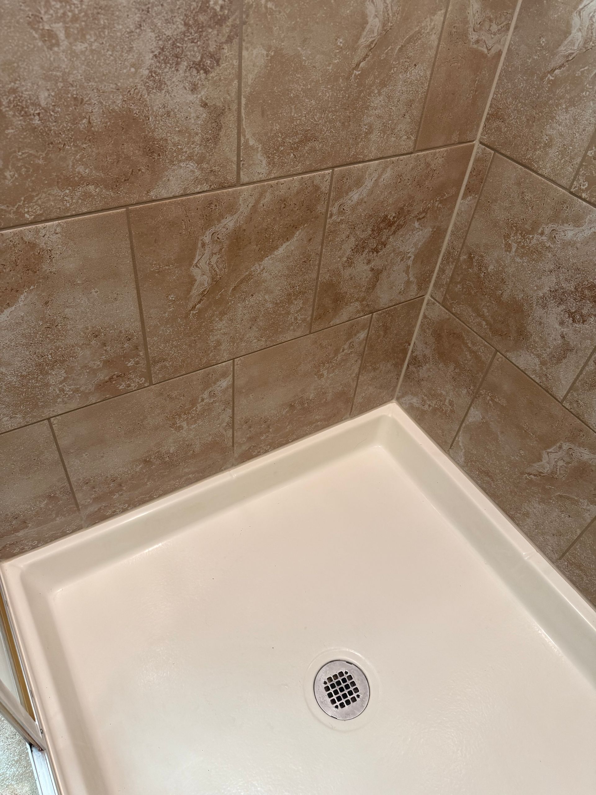 Beige tiled shower walls with a white shower basin and drain.
