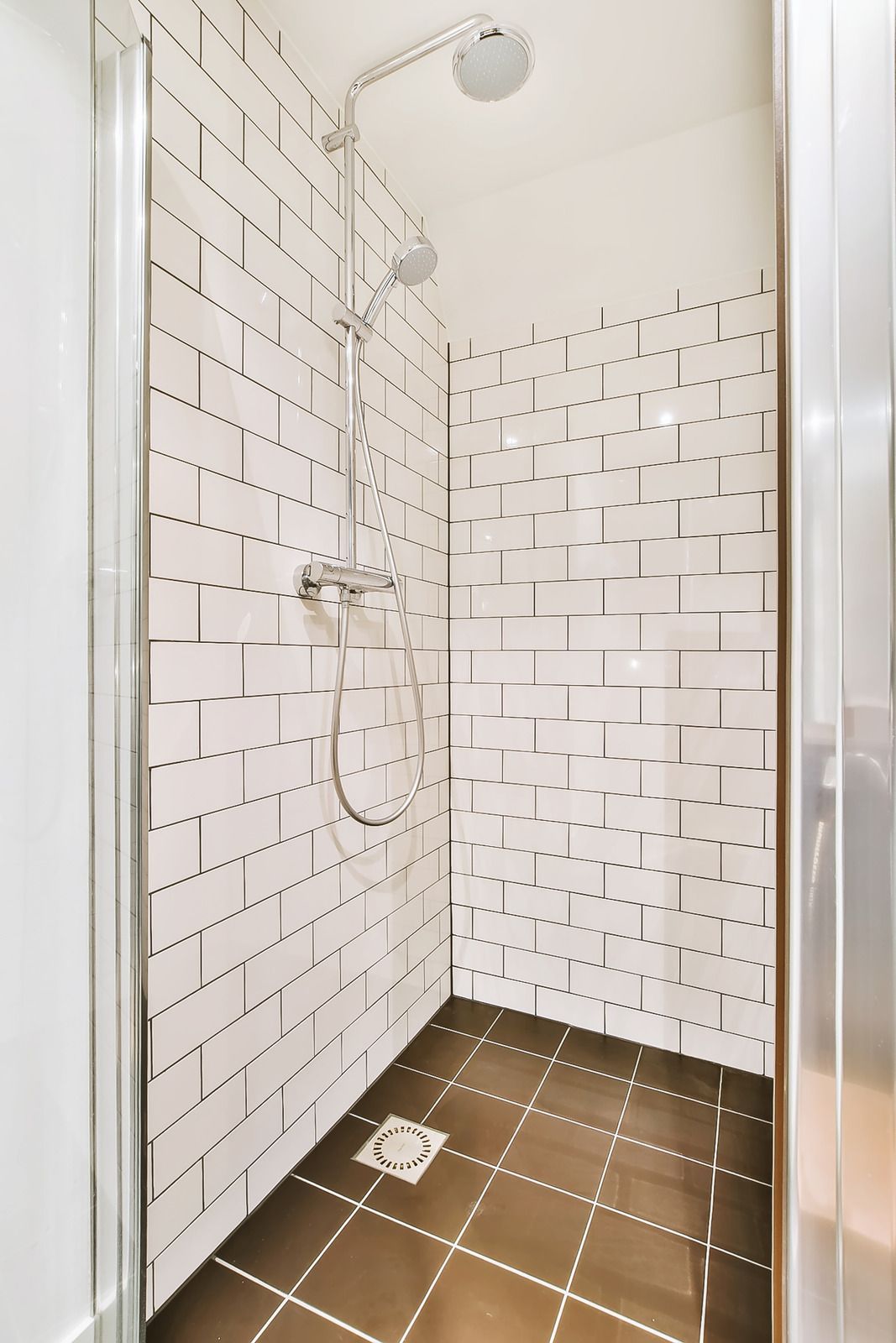 Shower with white subway tile walls and dark brown tile floor.