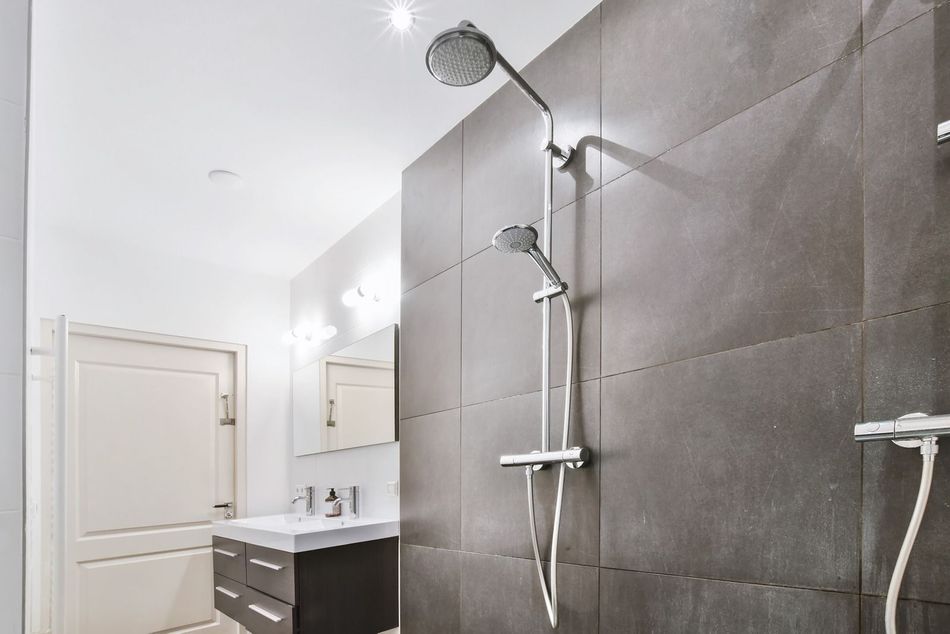 Modern bathroom with gray tiled shower, stainless steel shower fixtures, vanity, and a closed door.