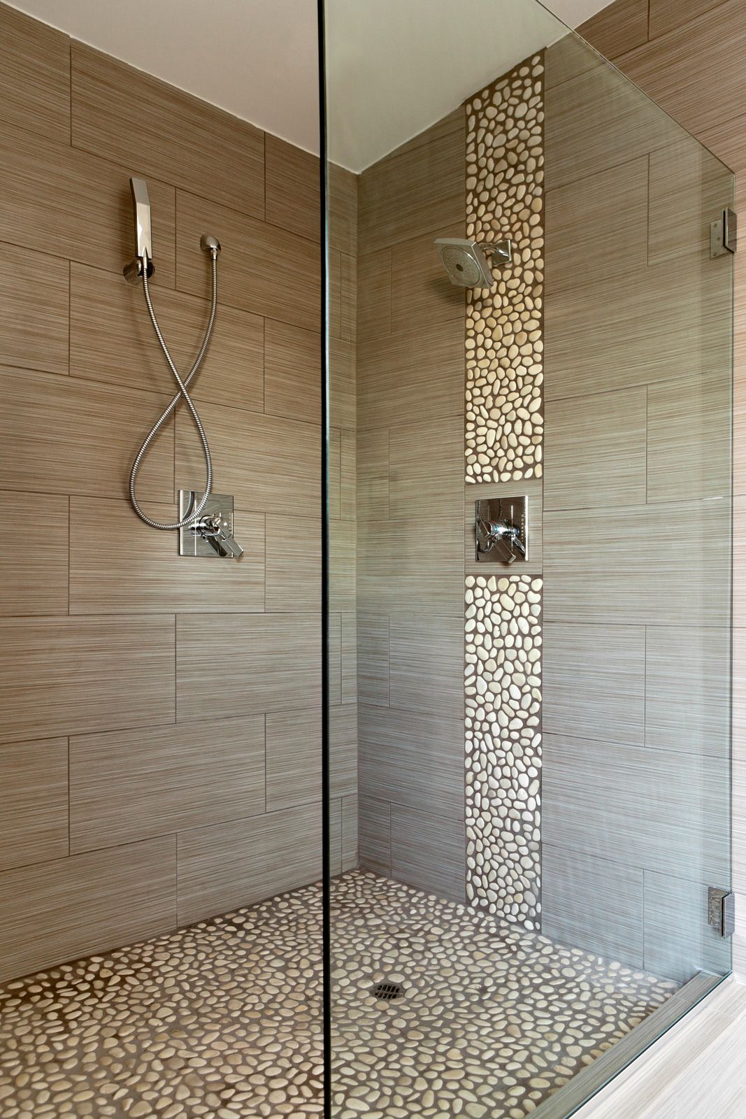 Shower with pebble tile floor, glass doors, and gray-brown tile walls.