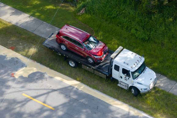 Red SUV on a flatbed tow truck next to a sidewalk and green grass.