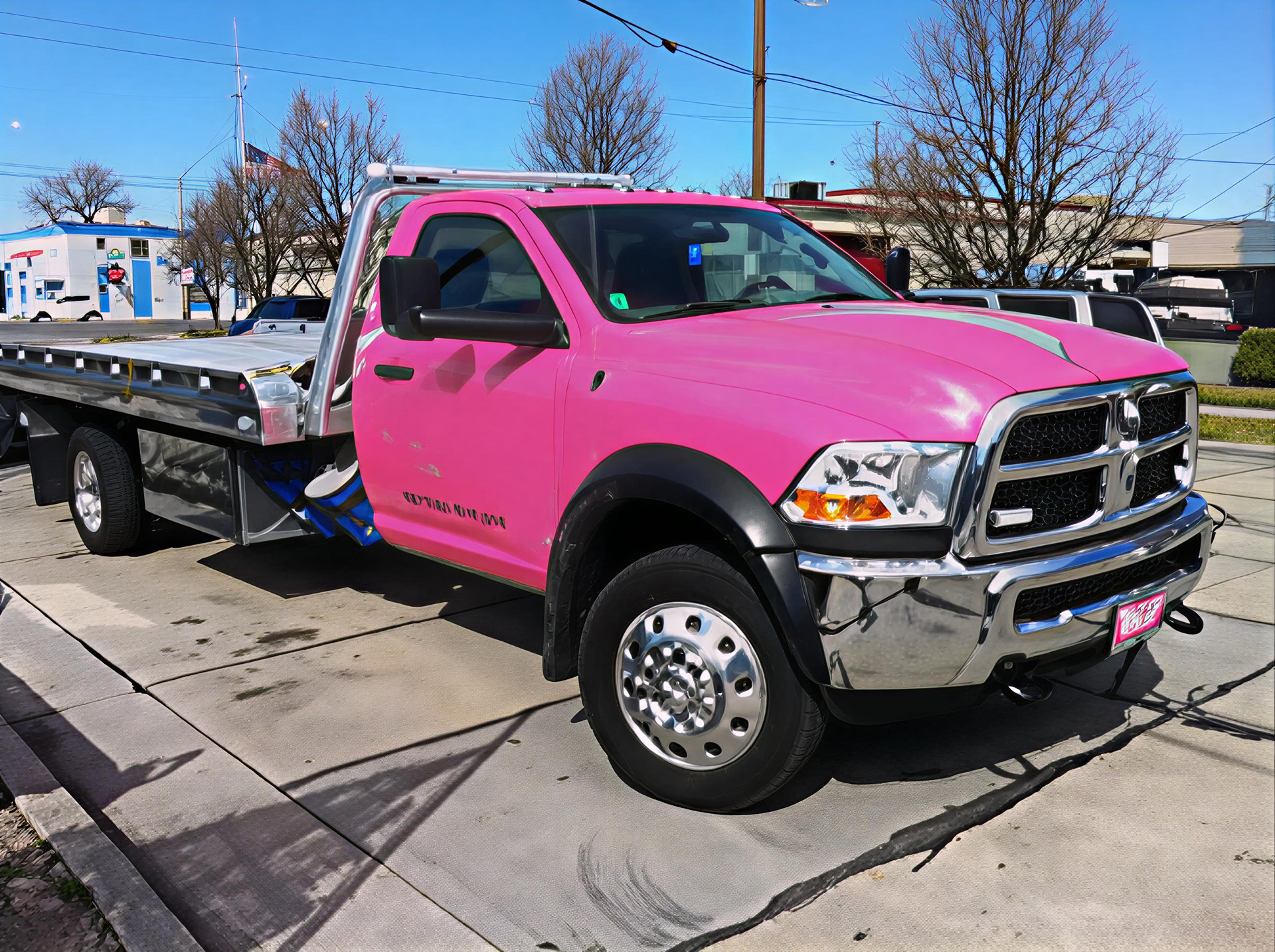 Pink tow truck parked on a paved lot in front of a building on a sunny day.