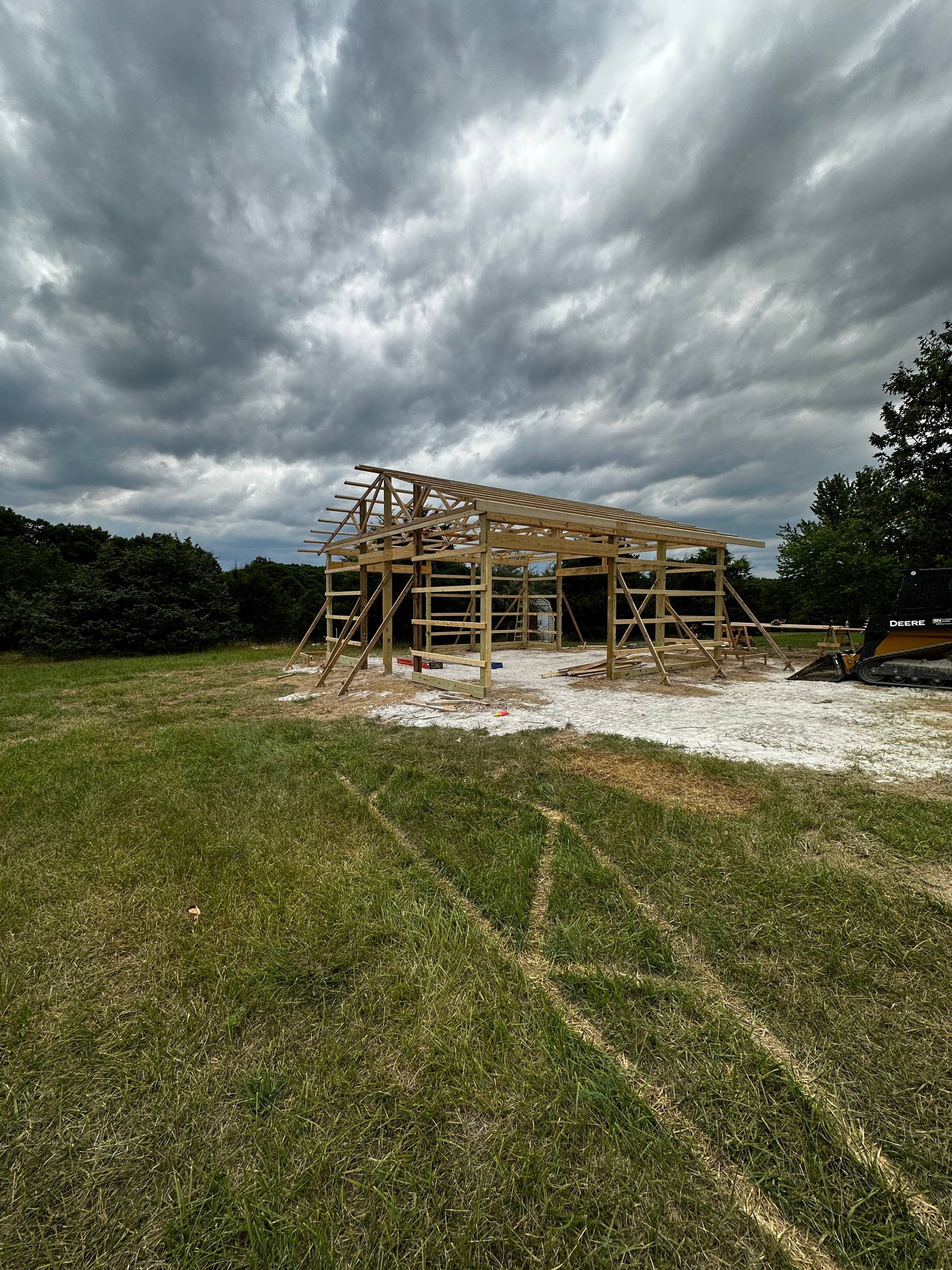 a wooden barn is being built in the middle of a grassy field .