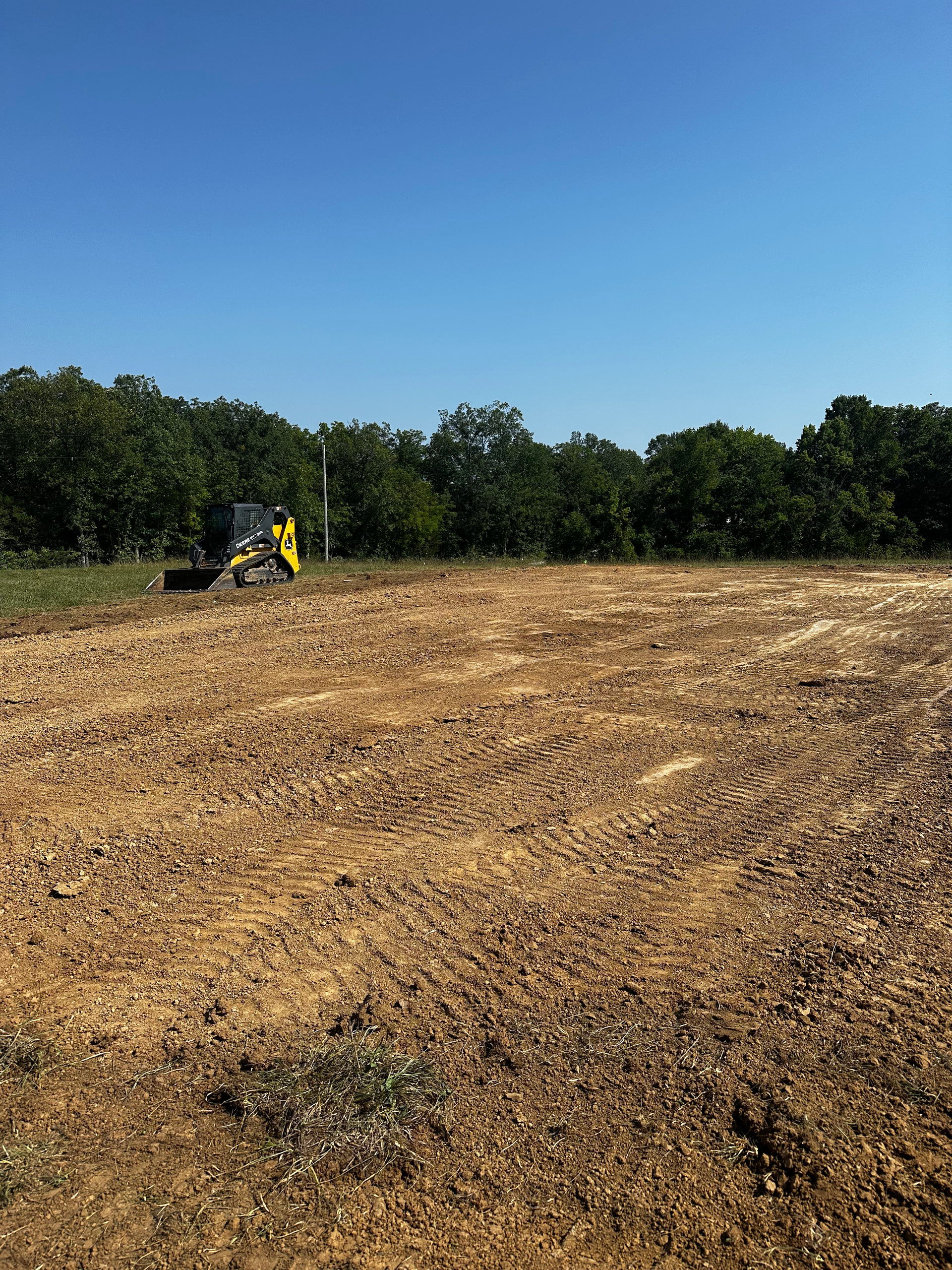 a bulldozer is driving through a dirt field with trees in the background .