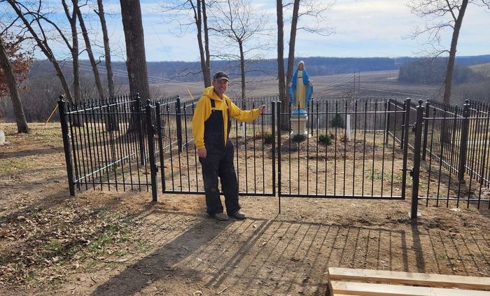 a man in a yellow jacket is standing in front of a wrought iron gate .