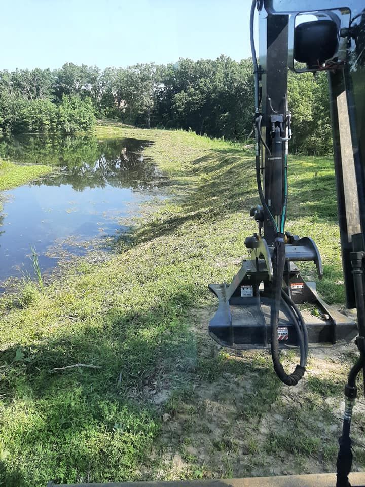 a tractor is cutting grass next to a pond in a field .