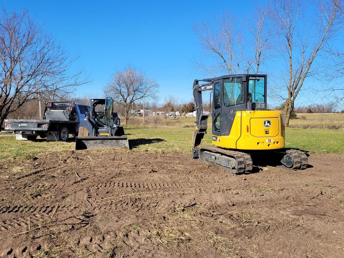 a yellow excavator is parked in a dirt field next to a truck .