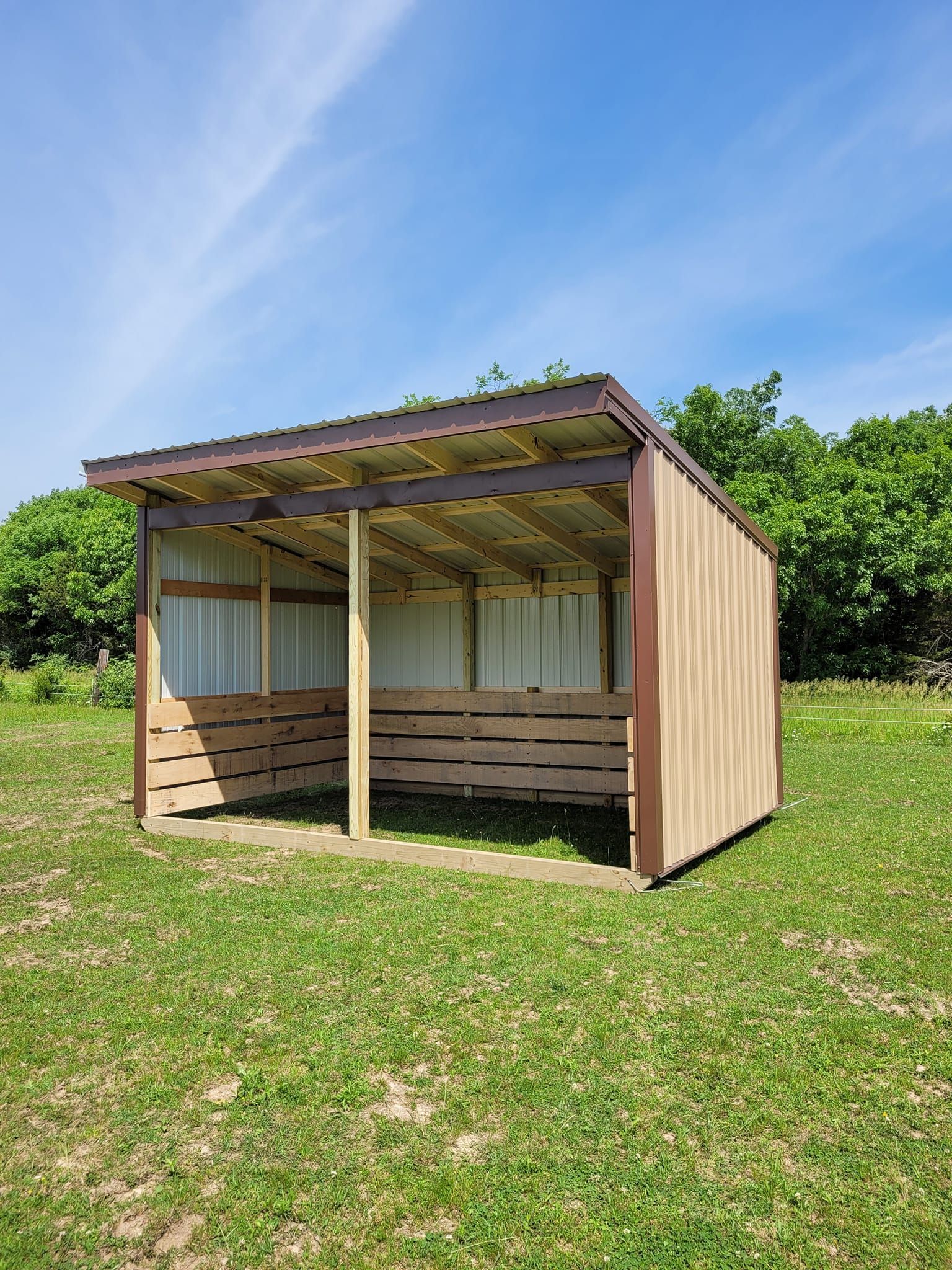 a small wooden shelter is sitting in the middle of a grassy field .