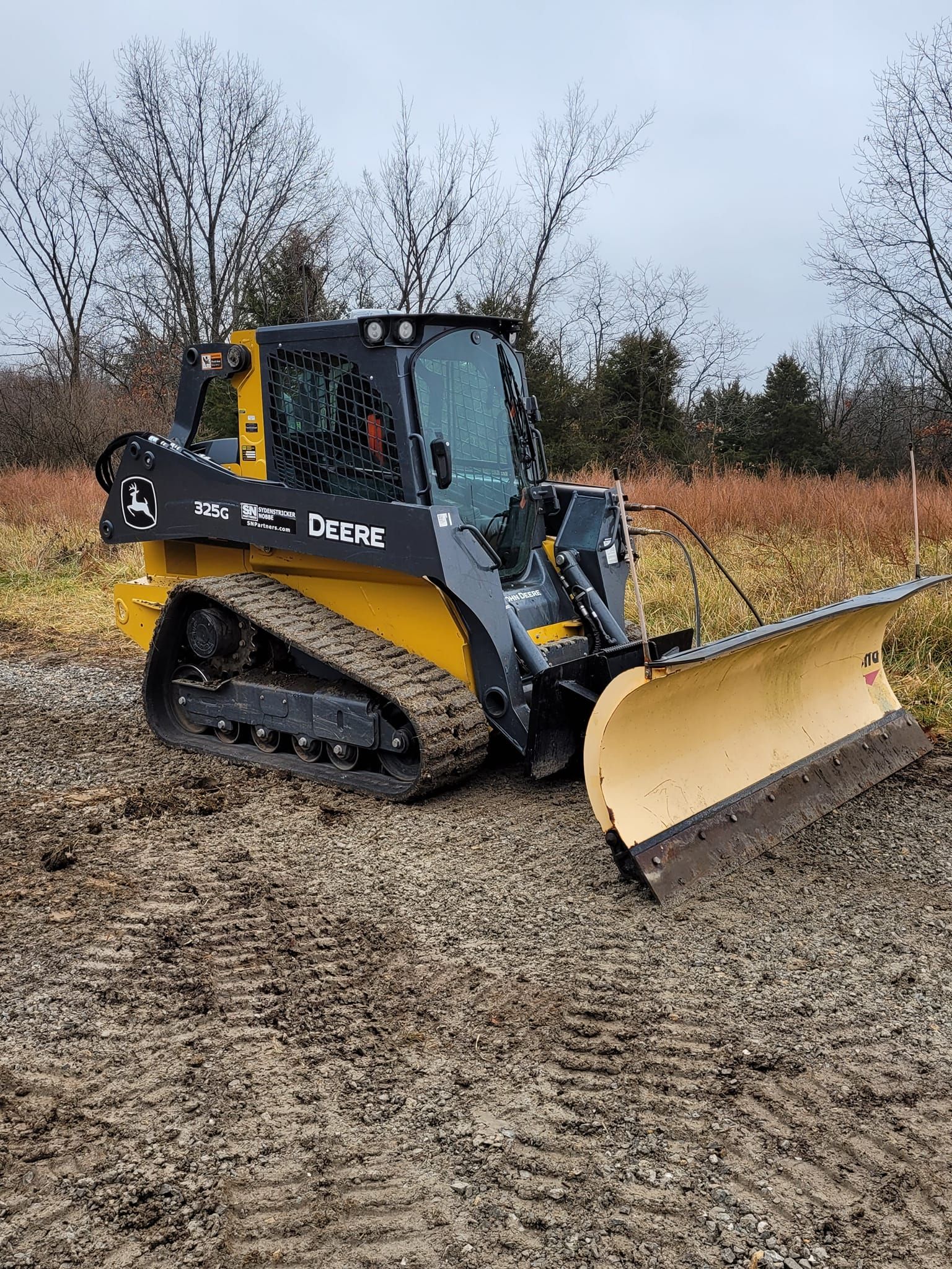 a bulldozer with a plow attached to it is driving through a muddy field .