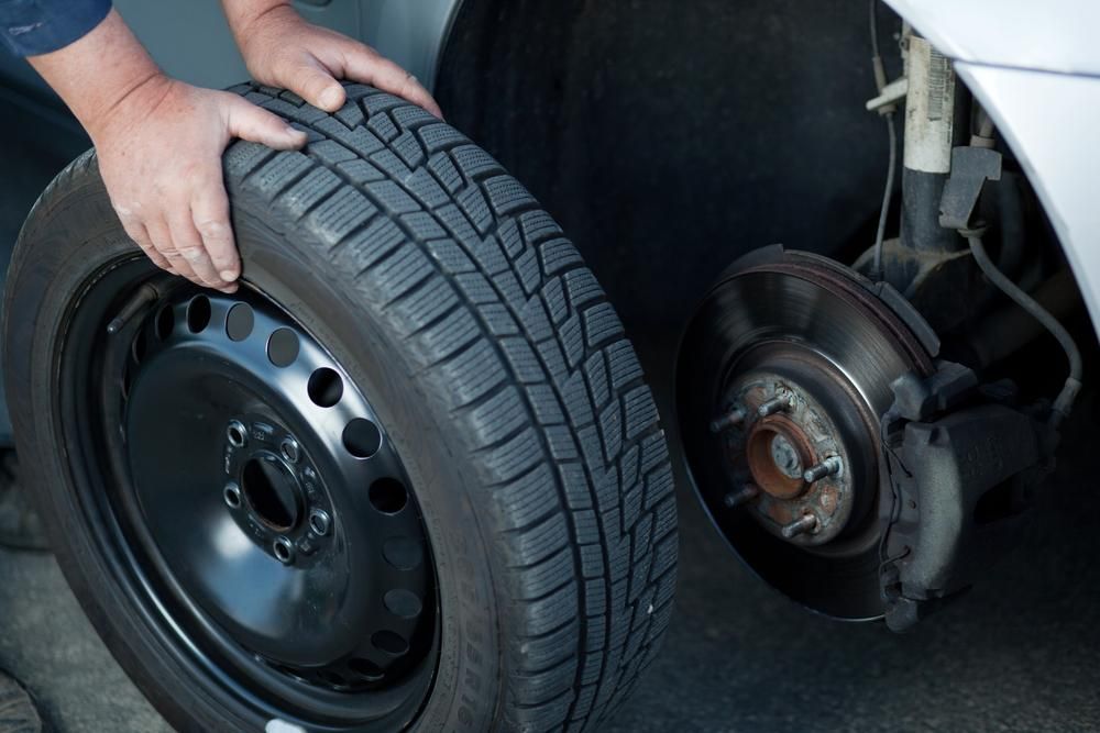 A Person Is Changing a Tire on A Car — Petersen's Second Hand & New Tyres in Currajong, QLD