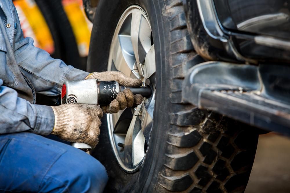 A Man Is Changing a Tire on A Car with A Wrench — Petersen's Second Hand & New Tyres in Currajong, QLD