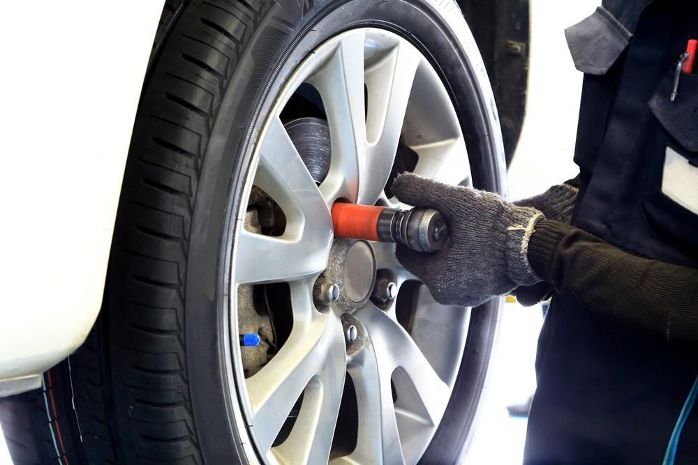 A Person Is Changing a Tire on A Car with A Wrench — Petersen's Second Hand & New Tyres in Currajong, QLD