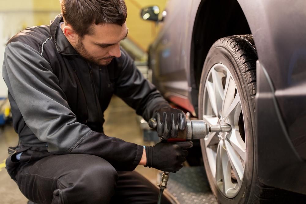 A Man Is Changing a Tire on A Car in A Garage — Petersen's Second Hand & New Tyres in Currajong, QLD