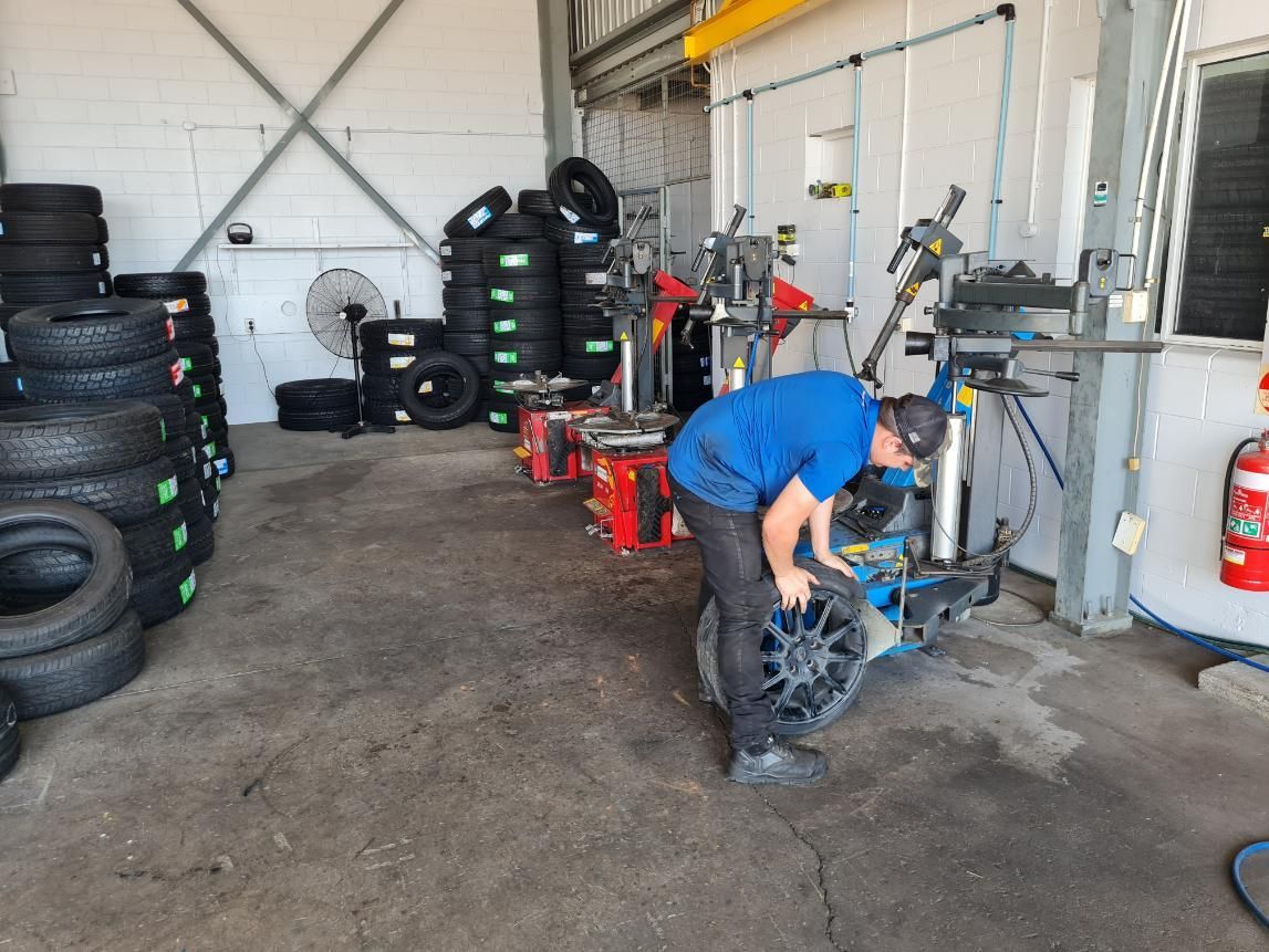 A Man Is Working on A Tire in A Garage — Petersen's Second Hand & New Tyres in Currajong, QLD