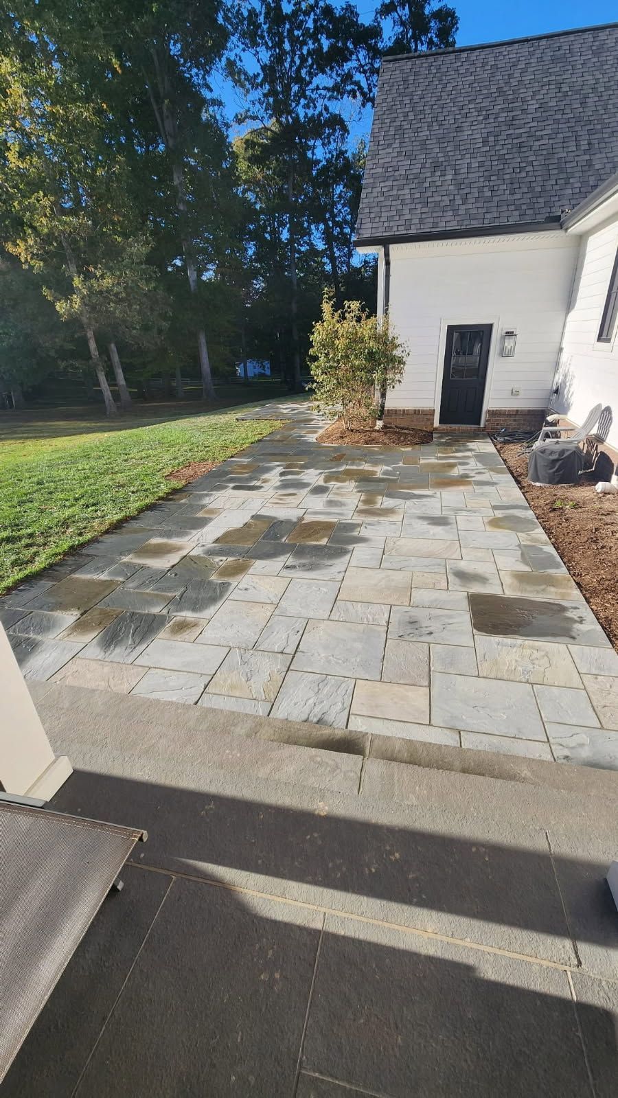 Patio with stone pavers next to a white house with a black door, wet from recent rain.