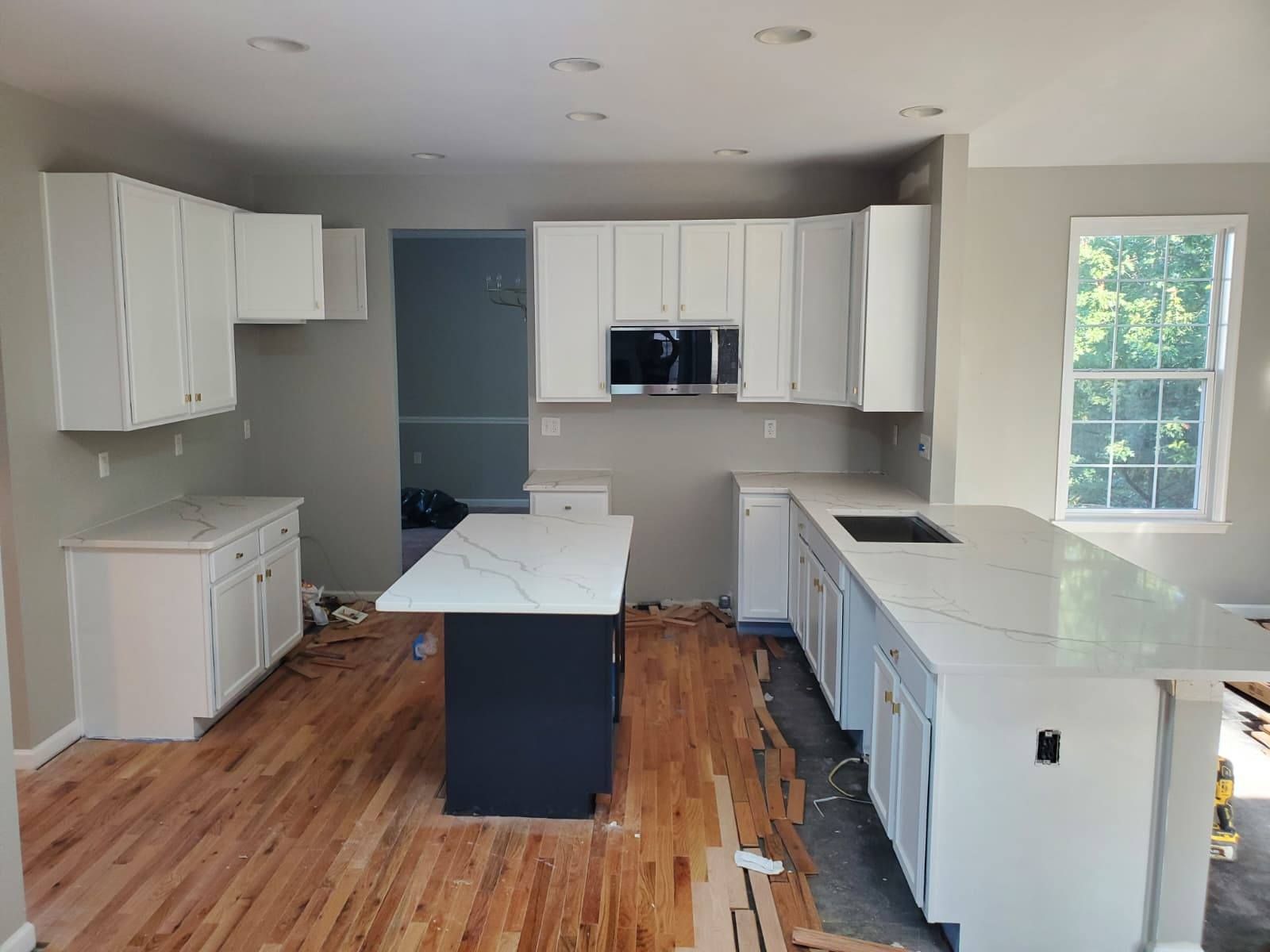 Kitchen remodel with white cabinets, dark island, and light countertops. Hardwood floors are damaged.