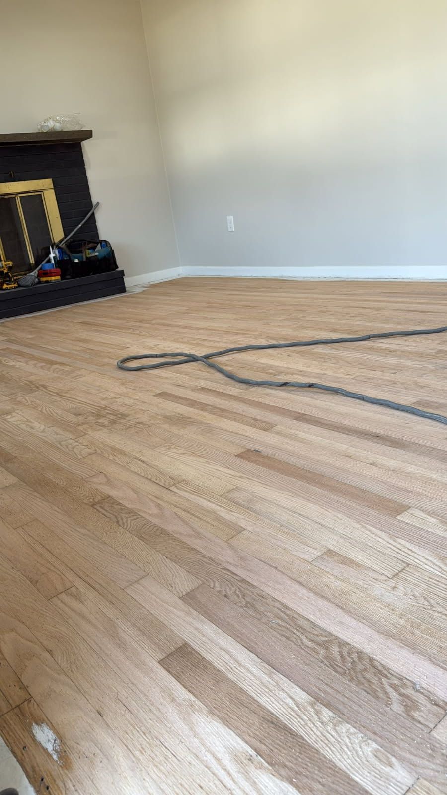 Wooden floor in a room, with a dark fireplace and a gray cord.