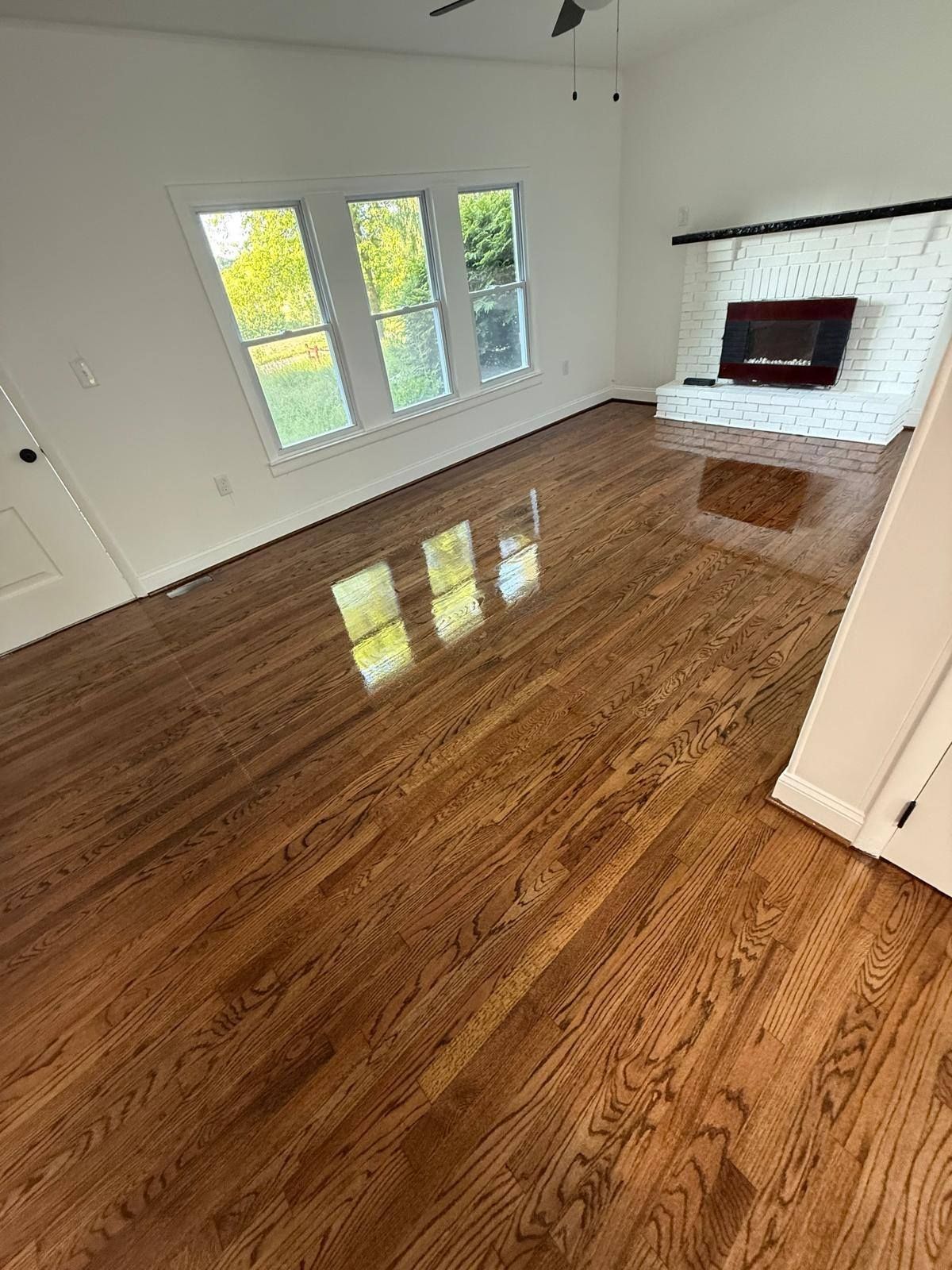 Hardwood floors reflect sunlight from windows in an open living area with a brick fireplace.