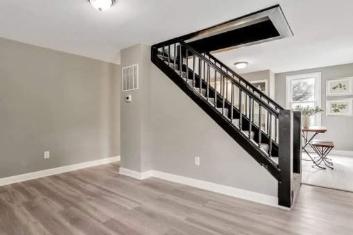 Gray-walled interior with black staircase, wooden floors, and a bright, open door at the top.