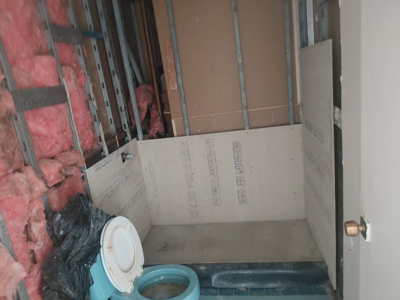 Bathroom under construction with exposed framing, insulation, and partially installed drywall. A toilet sits on the floor.