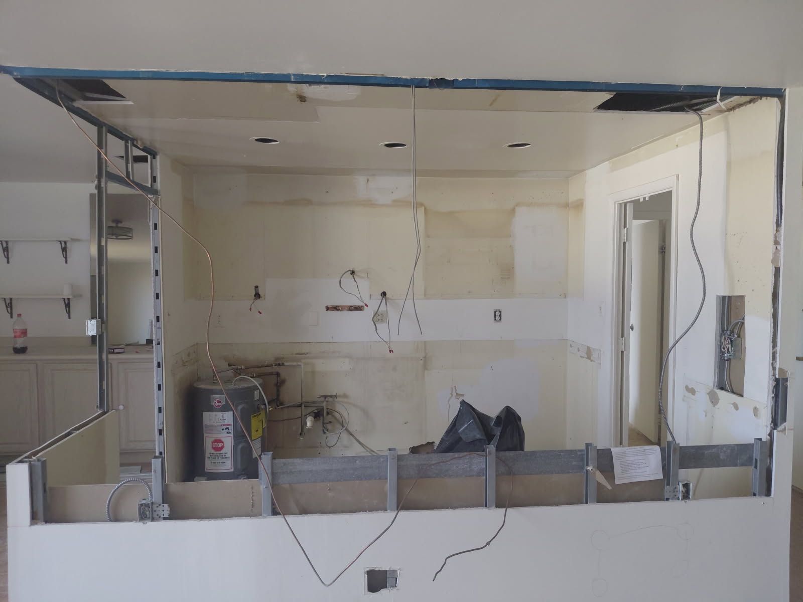 Kitchen under renovation; drywall removed, revealing framing, wires, and a water heater.