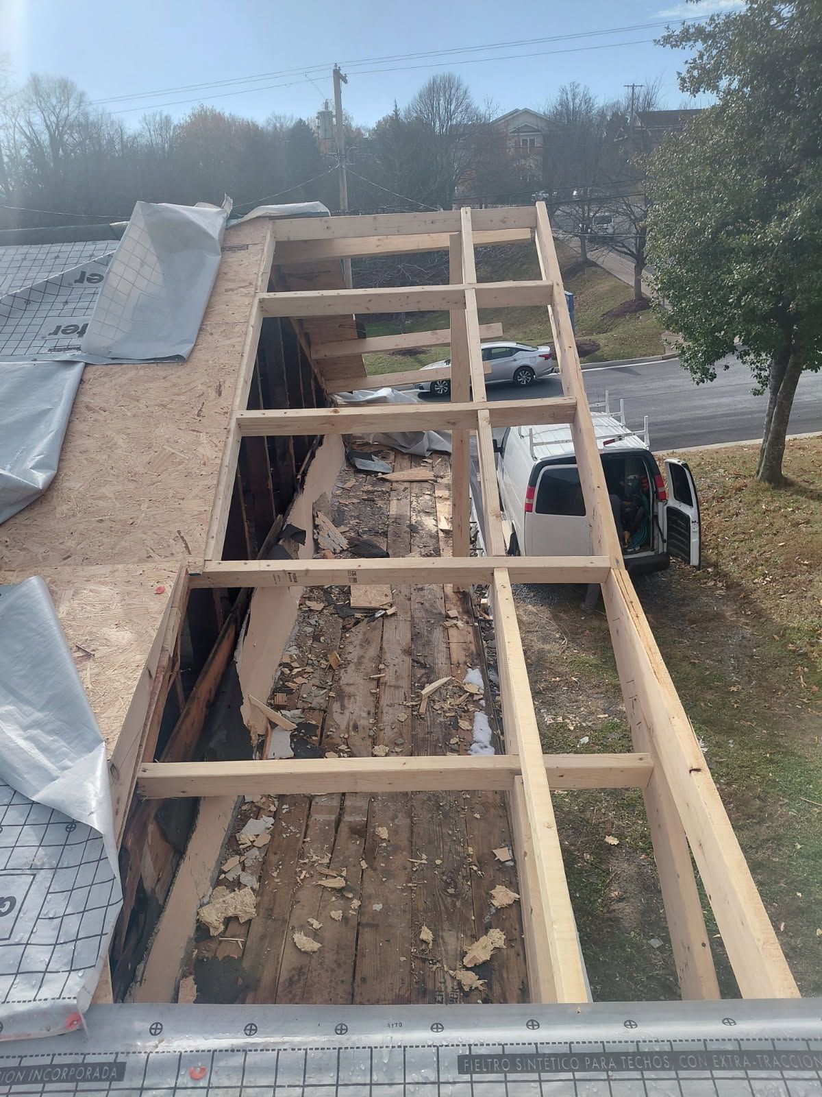 Roof under construction, with exposed wooden frame and old wood; a van is parked nearby.