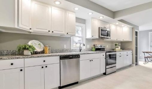 White kitchen with granite countertops and stainless steel appliances; a window in the center.