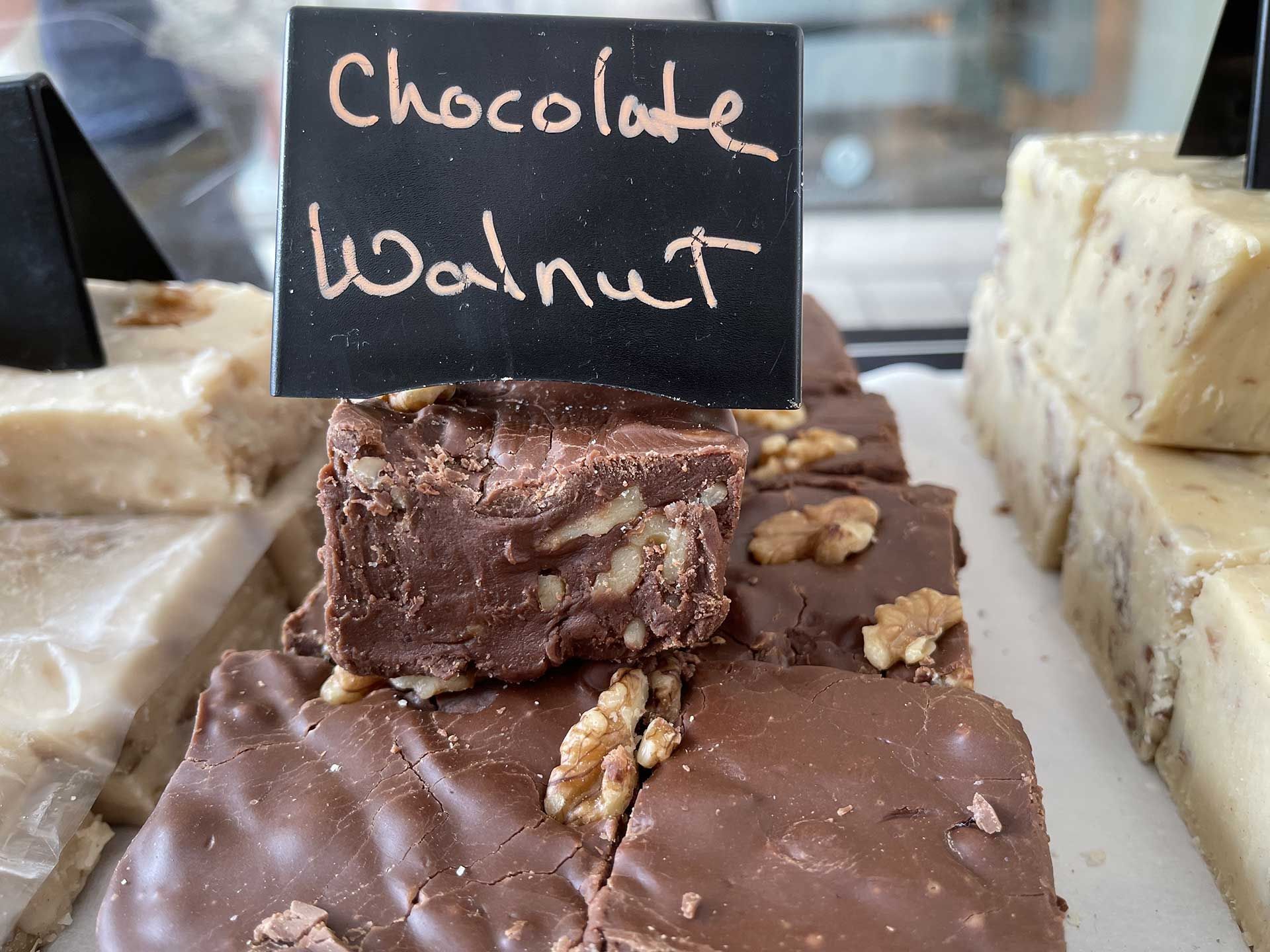 Chocolate walnut fudge squares with sign in bakery case.