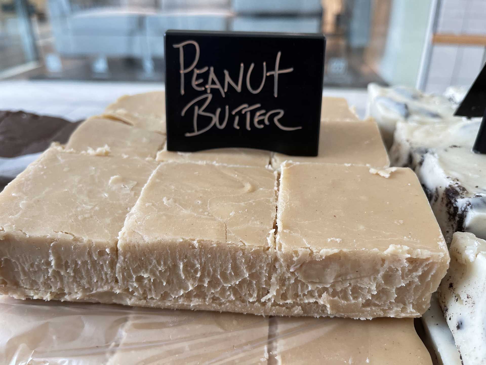 Peanut butter fudge, cut into squares, displayed in a shop. A black sign reads