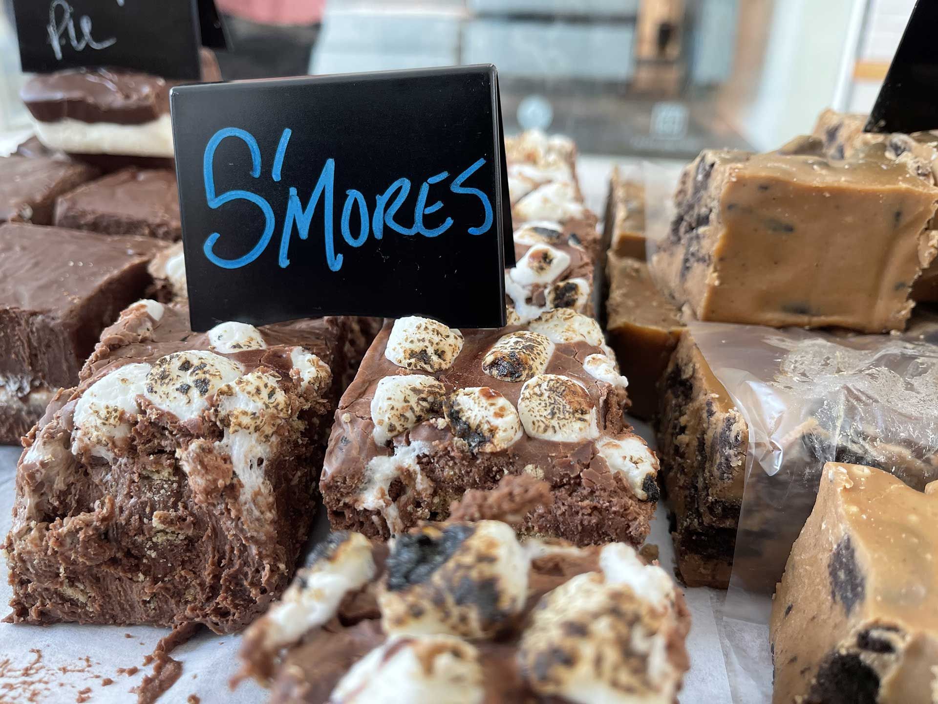 S'mores fudge squares topped with marshmallows, displayed at a sweets shop, with a