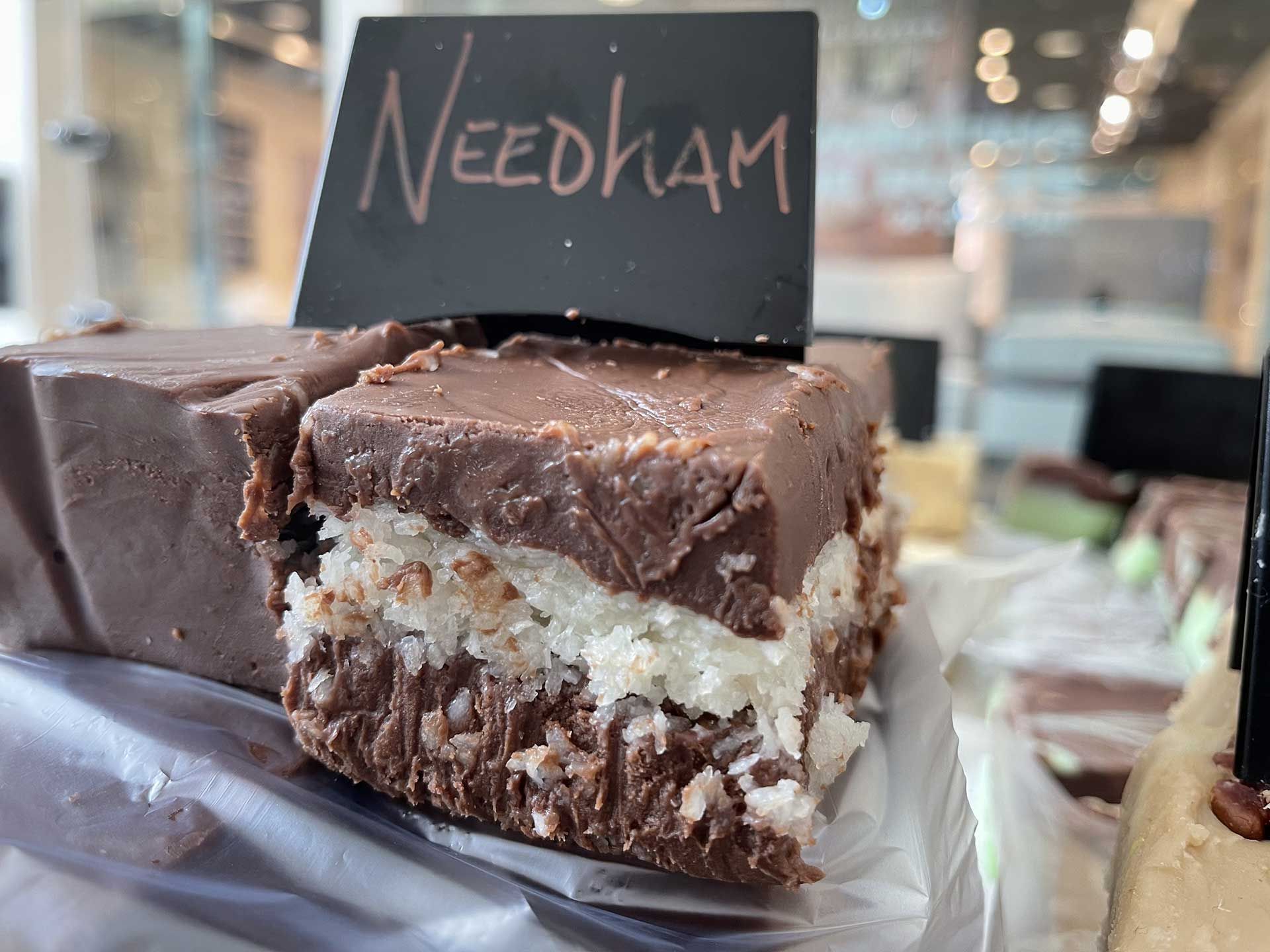 Needham fudge with chocolate frosting, coconut layer, and chocolate base. Black sign.