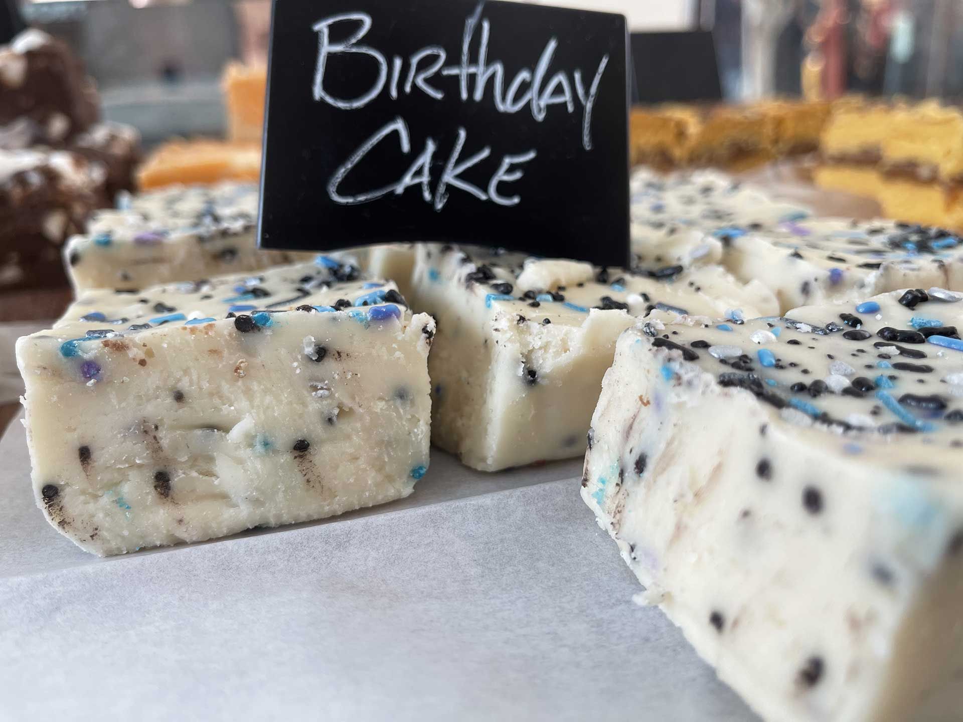 Birthday cake fudge squares with blue and black sprinkles, on display.