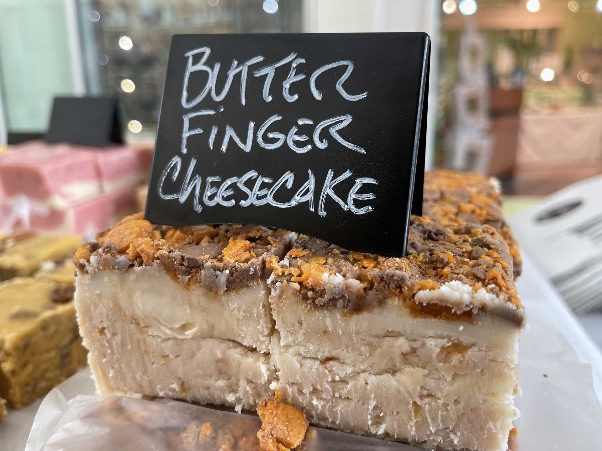 Butterfinger cheesecake slice with a black sign, on a white plate.