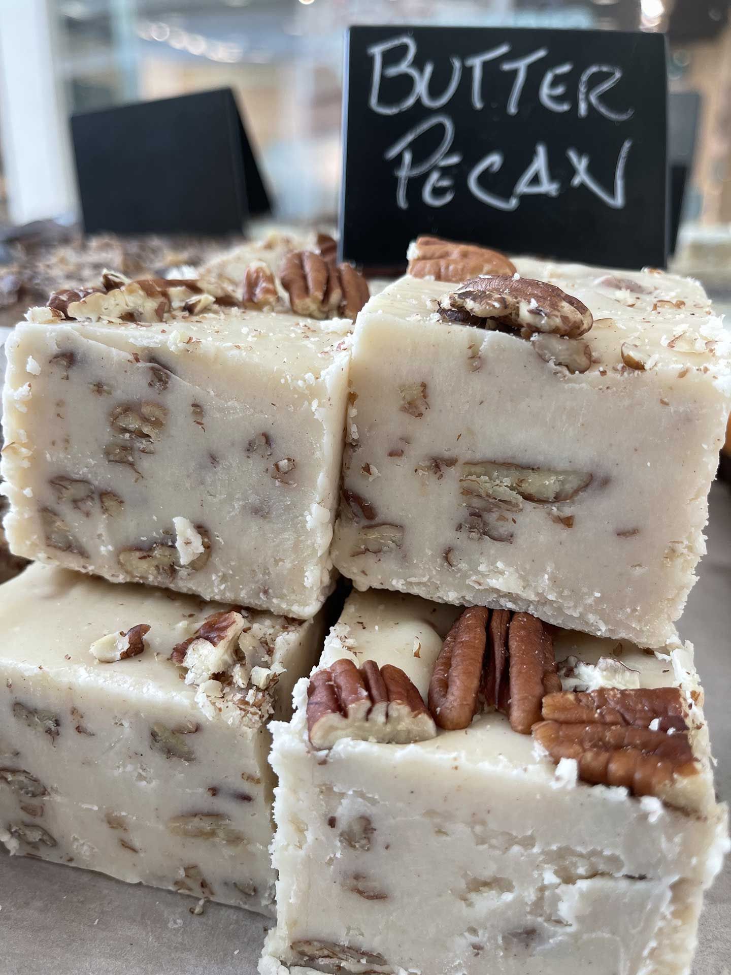 Butter pecan fudge squares topped with pecans, stacked in a bakery setting.