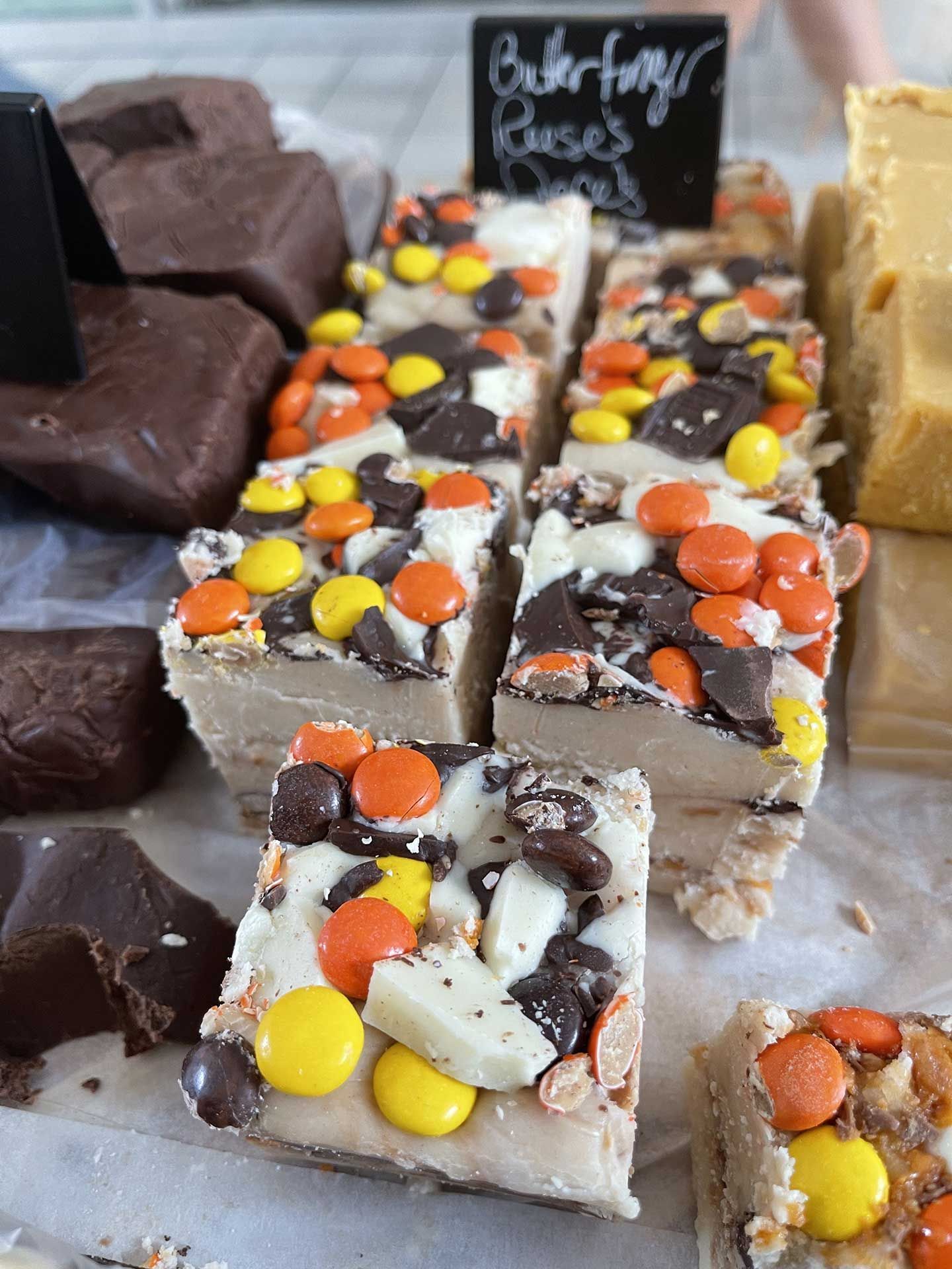 Fudge squares with Reese's Pieces, chocolate chips, and nuts at a bakery, next to dark and tan fudge.