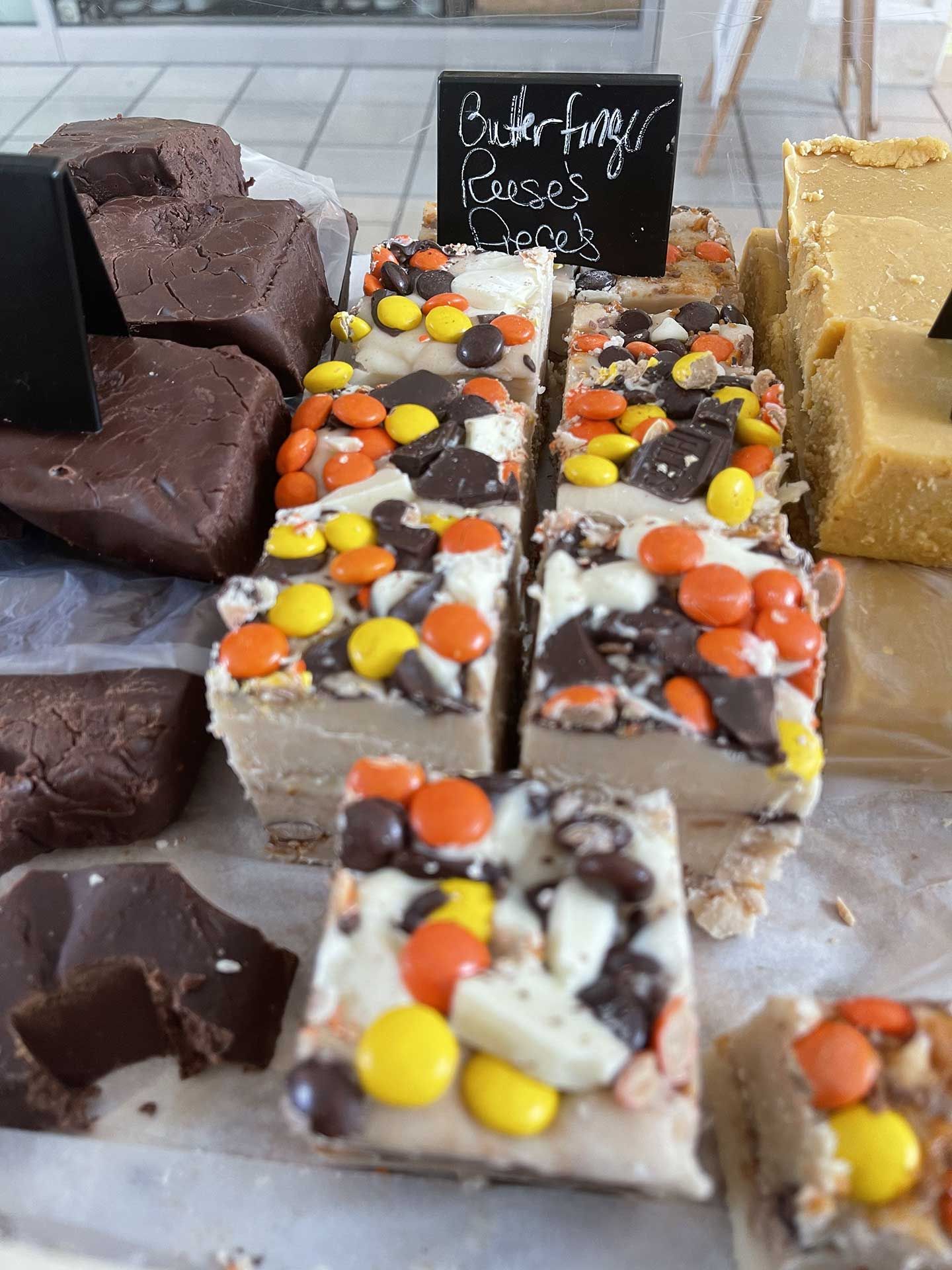 Fudge display: blocks of chocolate, peanut butter, and Reese's pieces fudge on white paper.