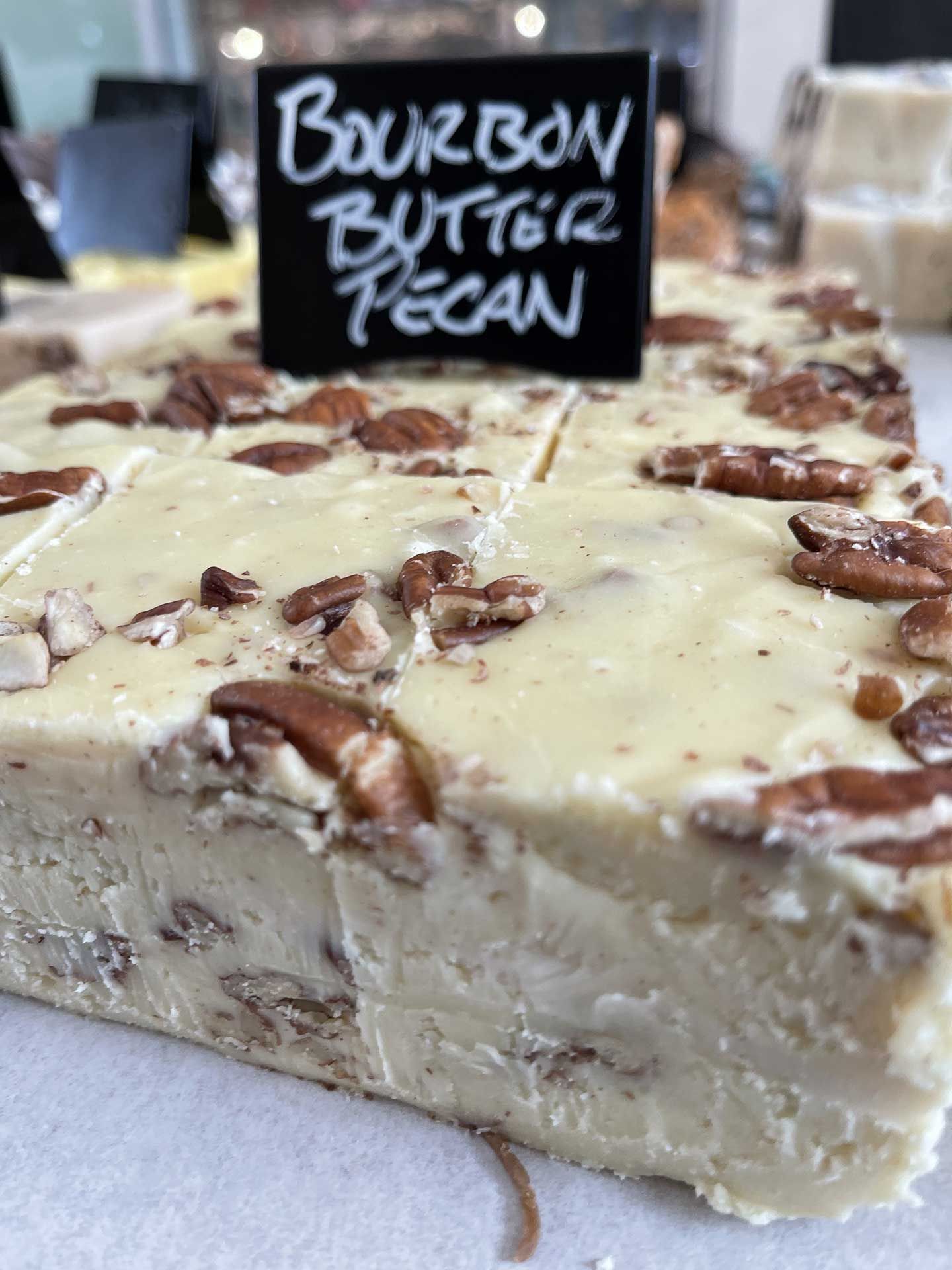 Bourbon butter pecan fudge with pecan pieces, white frosting, and a black sign that says