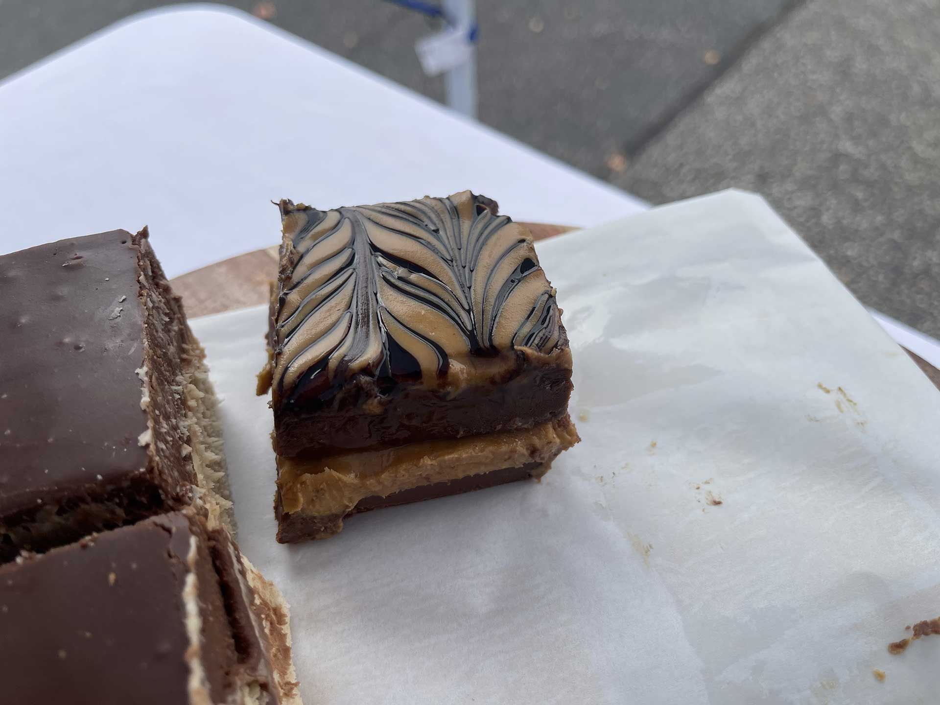 A square brownie with peanut butter filling and swirled chocolate topping, on a white paper.
