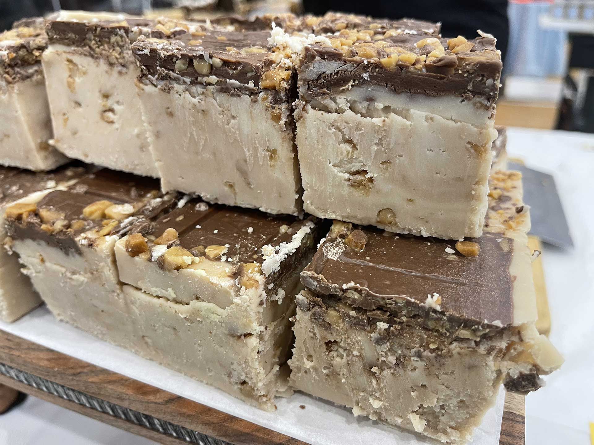 Stack of fudge squares, light brown base with chocolate topping, sprinkled with nuts.