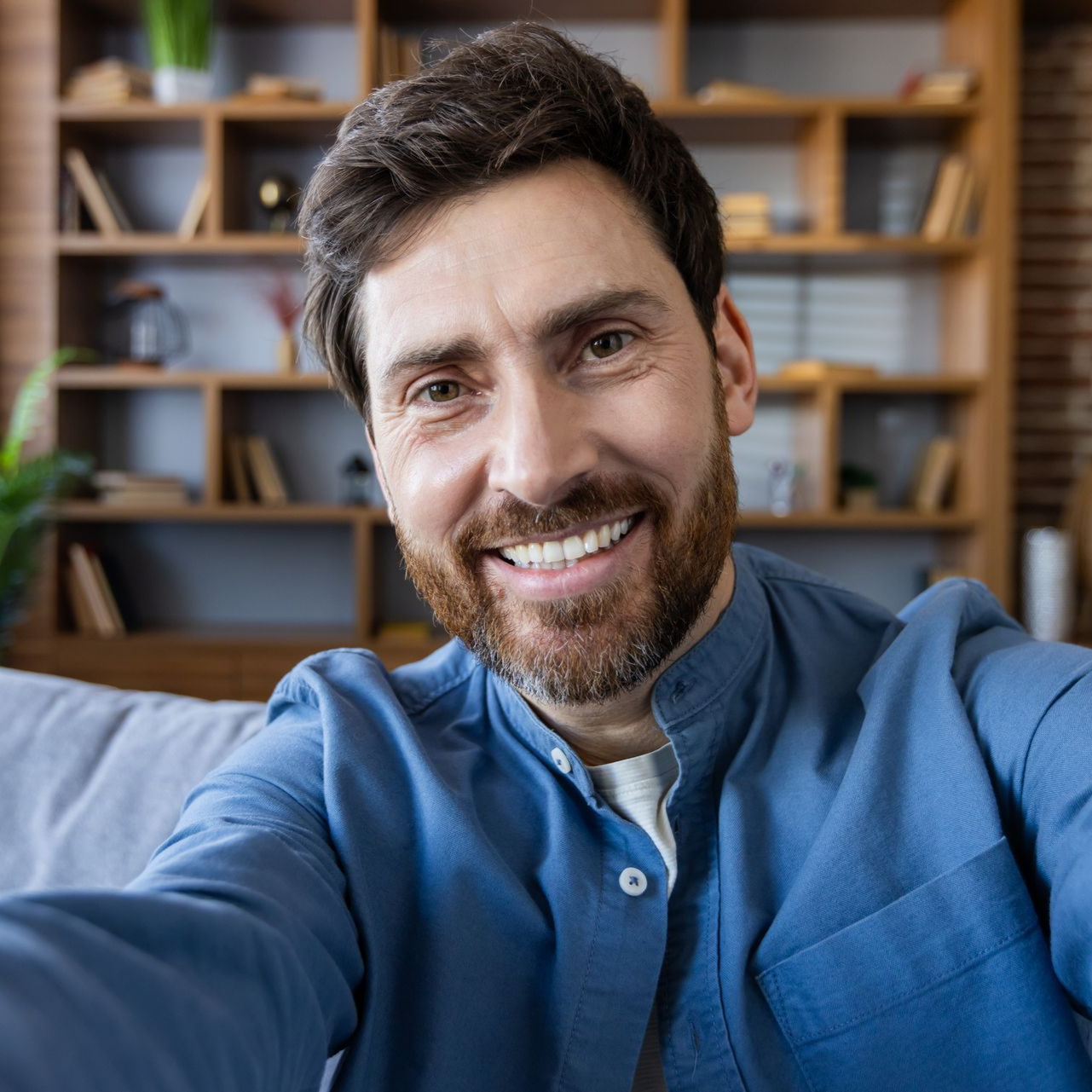 Man smiling, taking selfie, holding camera, inside home, modern decor.