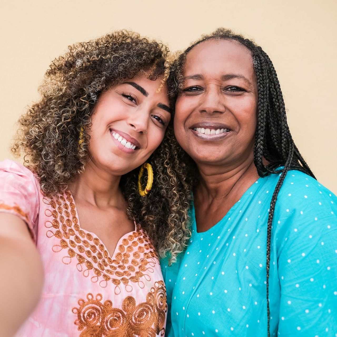 Woman with curly hair, pink dress, smiling next to older woman with braided hair in blue. Both smiling.