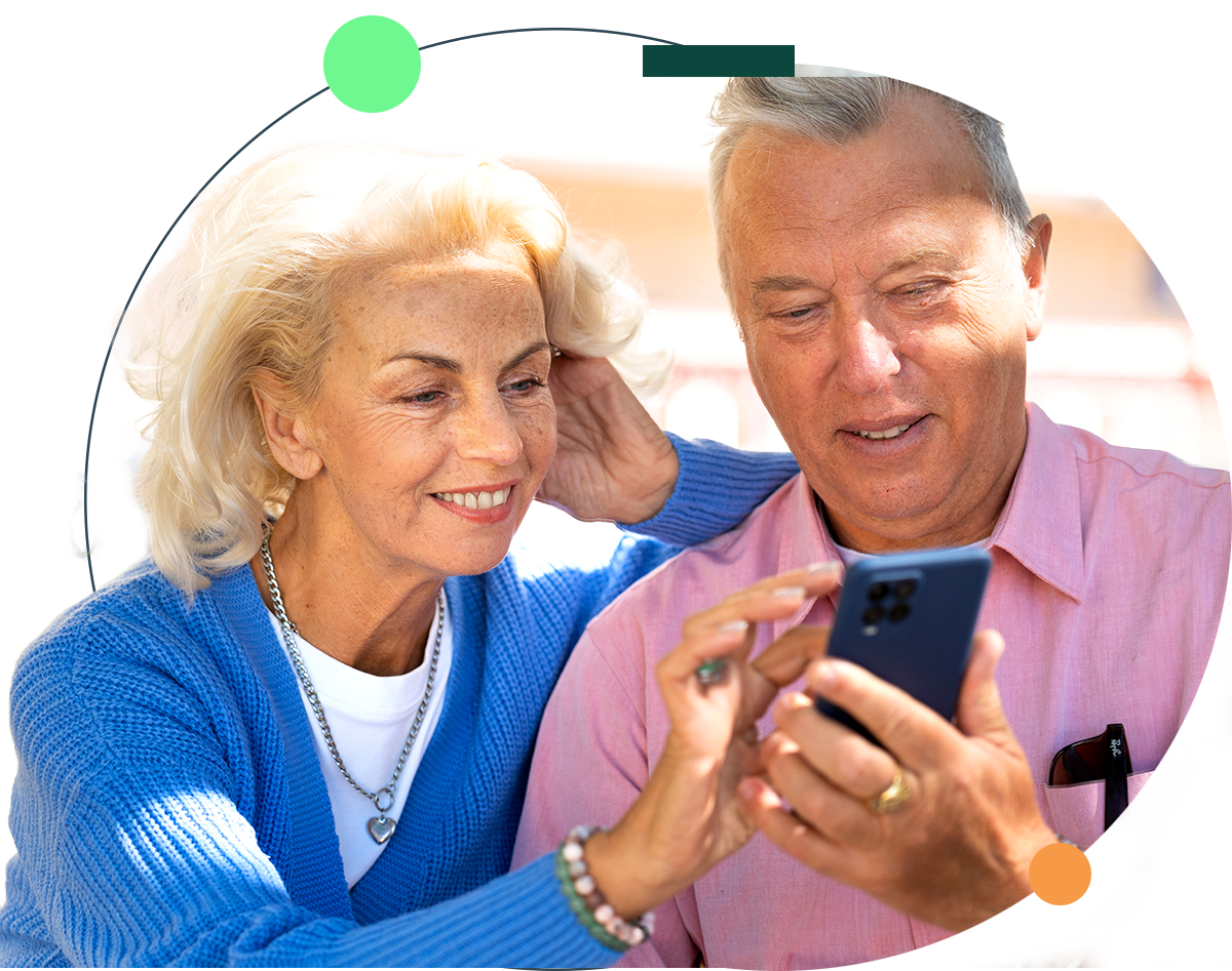 Senior man with glasses using a laptop, smiling, at a cafe table with a coffee cup.