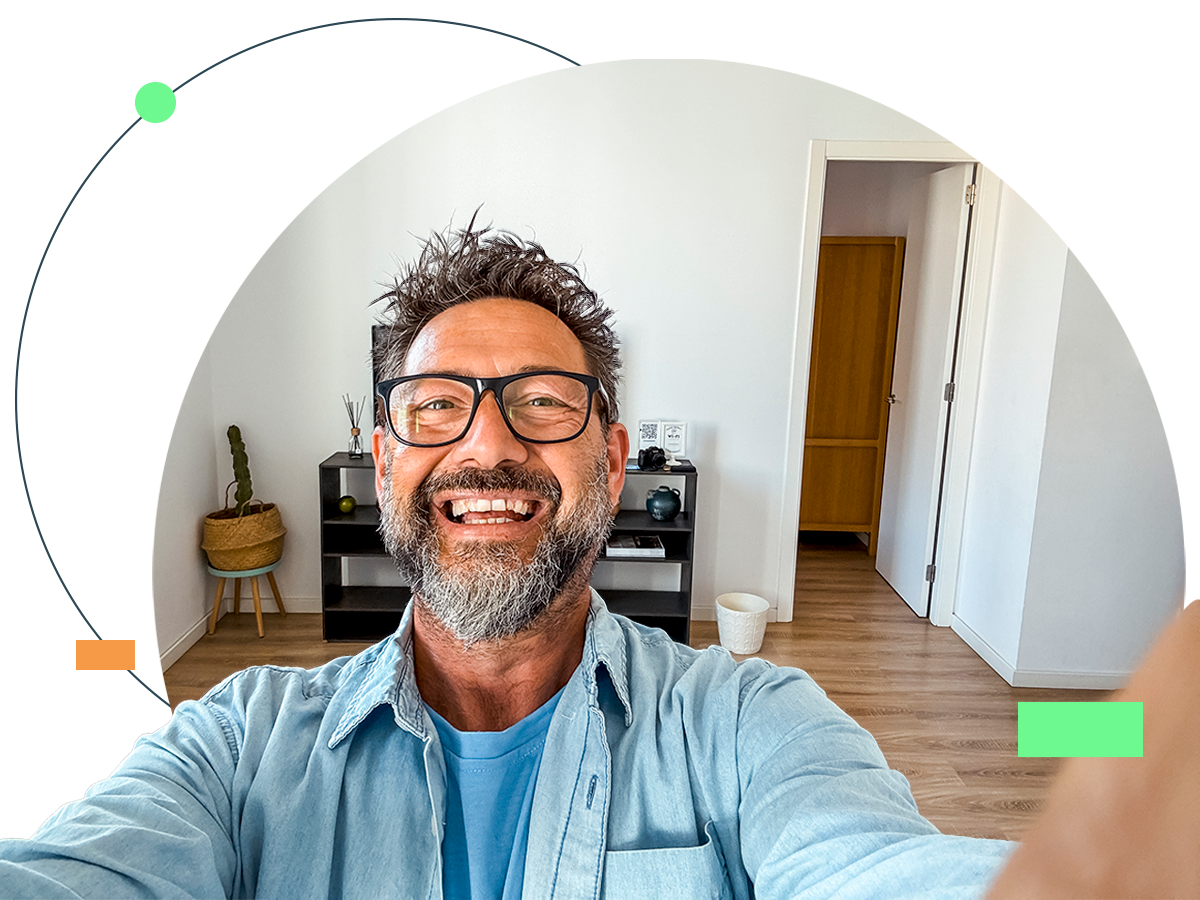 Man smiling, taking selfie, holding camera, inside home, modern decor.