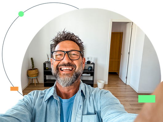 Man smiling, taking selfie, holding camera, inside home, modern decor.